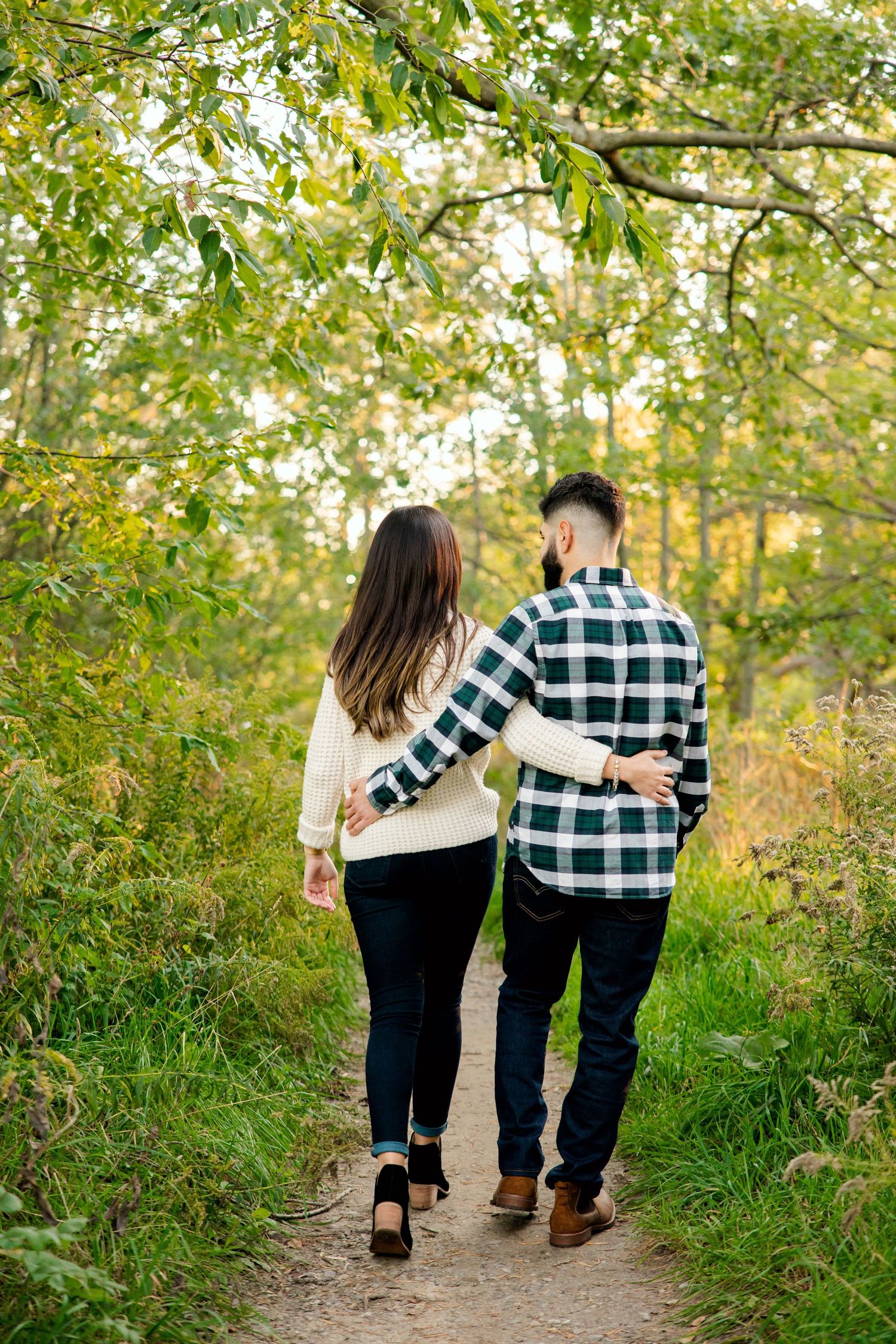 Couple walking arm in arm down a forest trail in autumn.