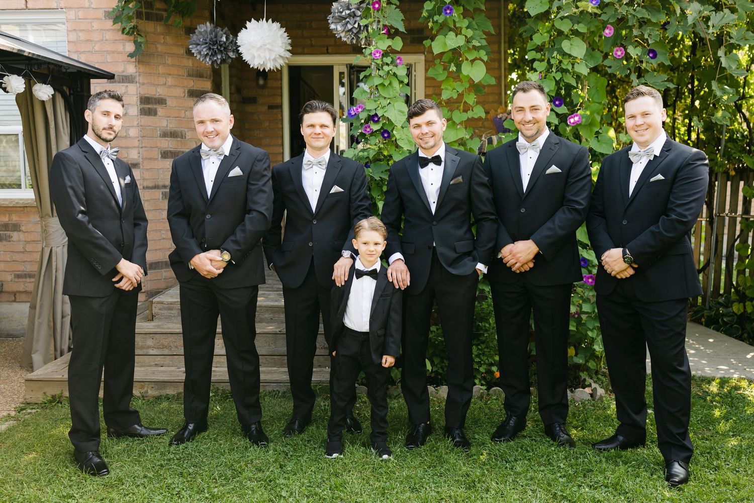 Groomsmen and young ring bearer in matching tuxedos lined up for formal wedding photo.