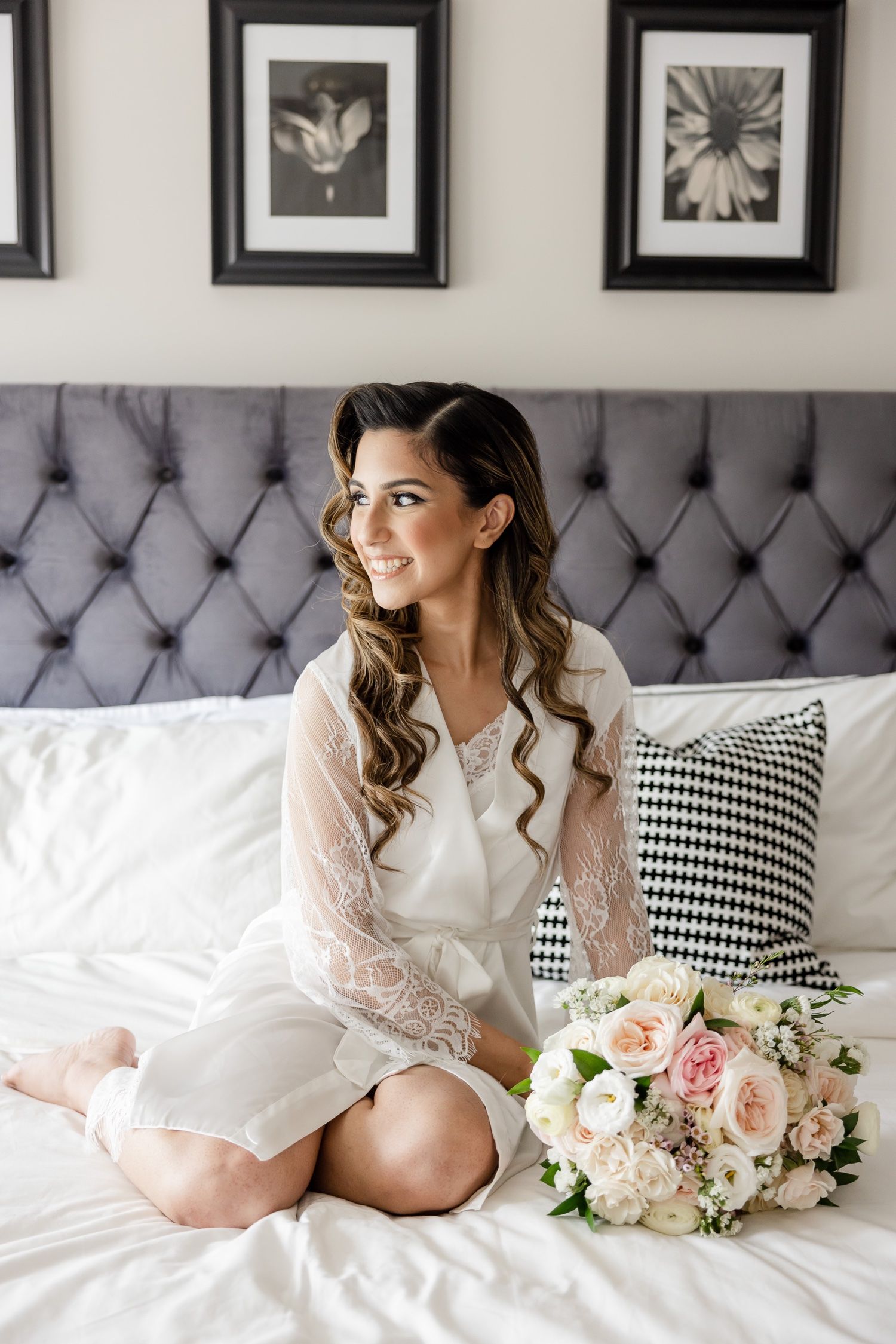 Elegant bridal boudoir scene with white robe, floral bouquet and gray tufted headboard.