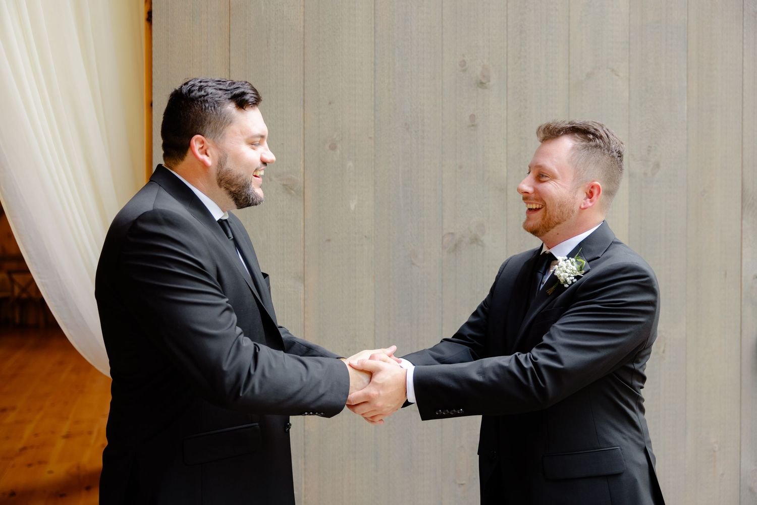 Two people in black suits shake hands during formal occasion.