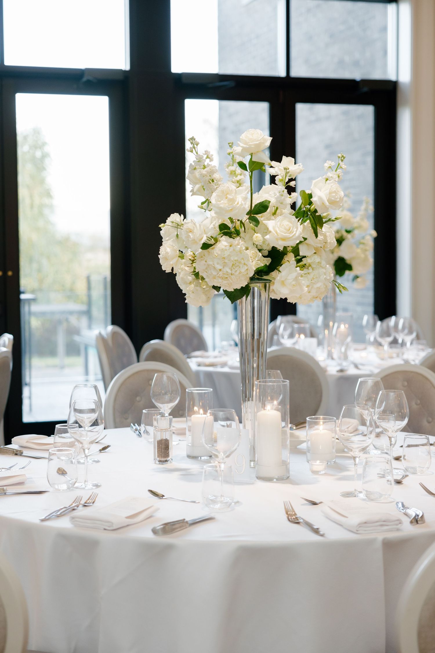Elegant white wedding reception table setting with tall floral centerpiece and crystal glassware at The Regency.