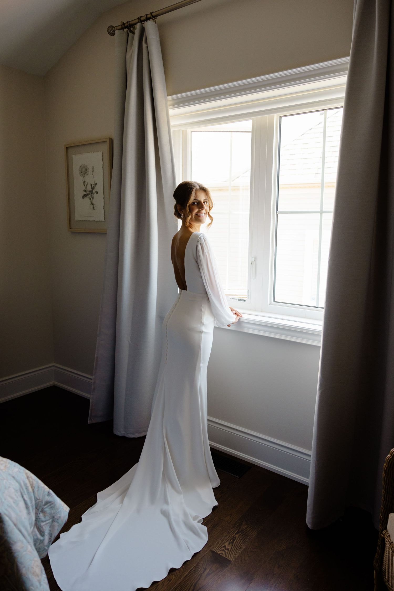 Bridal portrait showing the dramatic train of a sleek white wedding gown near a window.