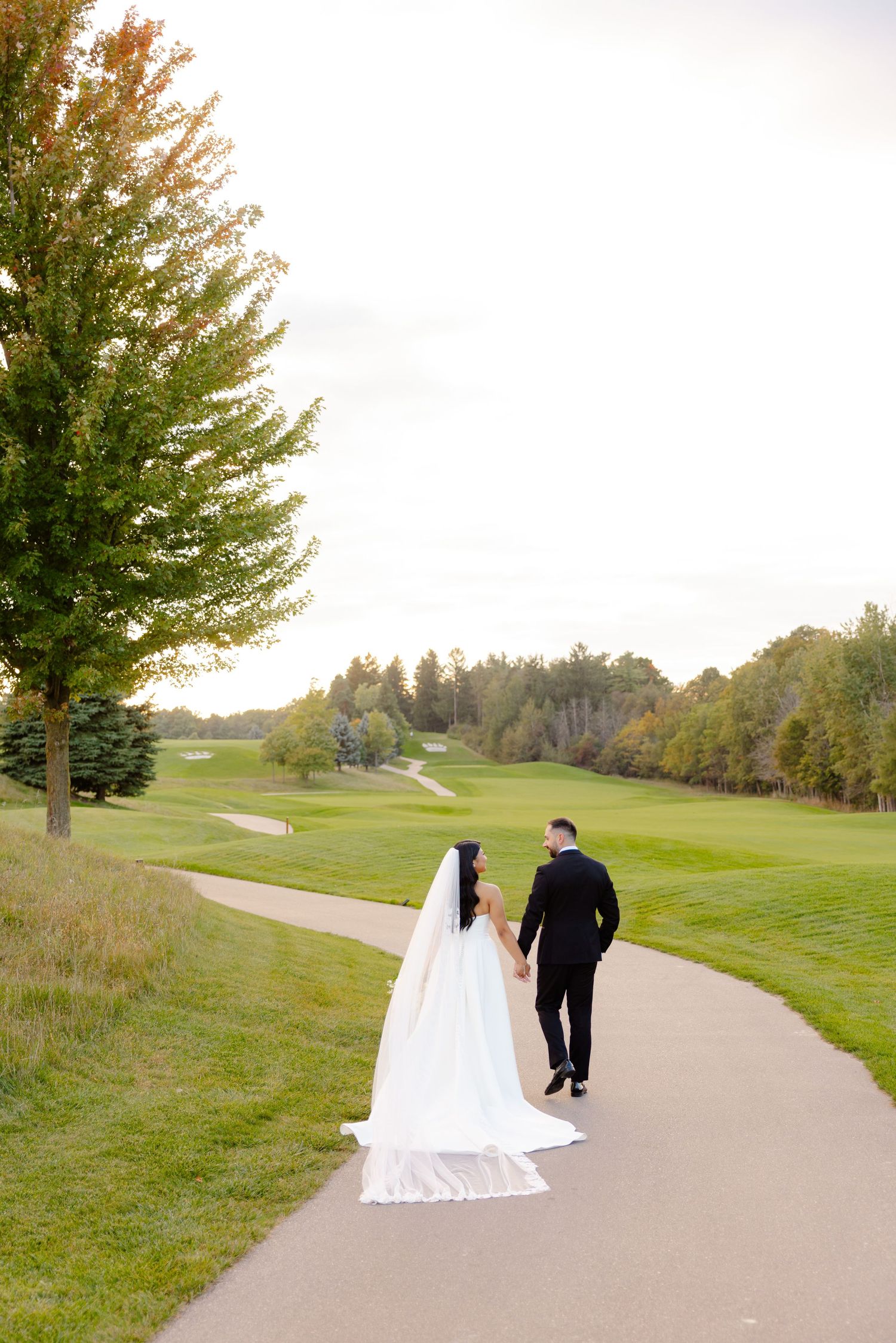 Wedding couple walking along a scenic golf course path with a flowing white dress train.