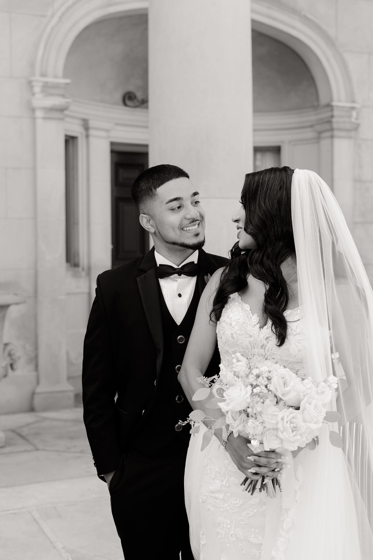 A romantic black and white wedding portrait captured under an elegant archway.