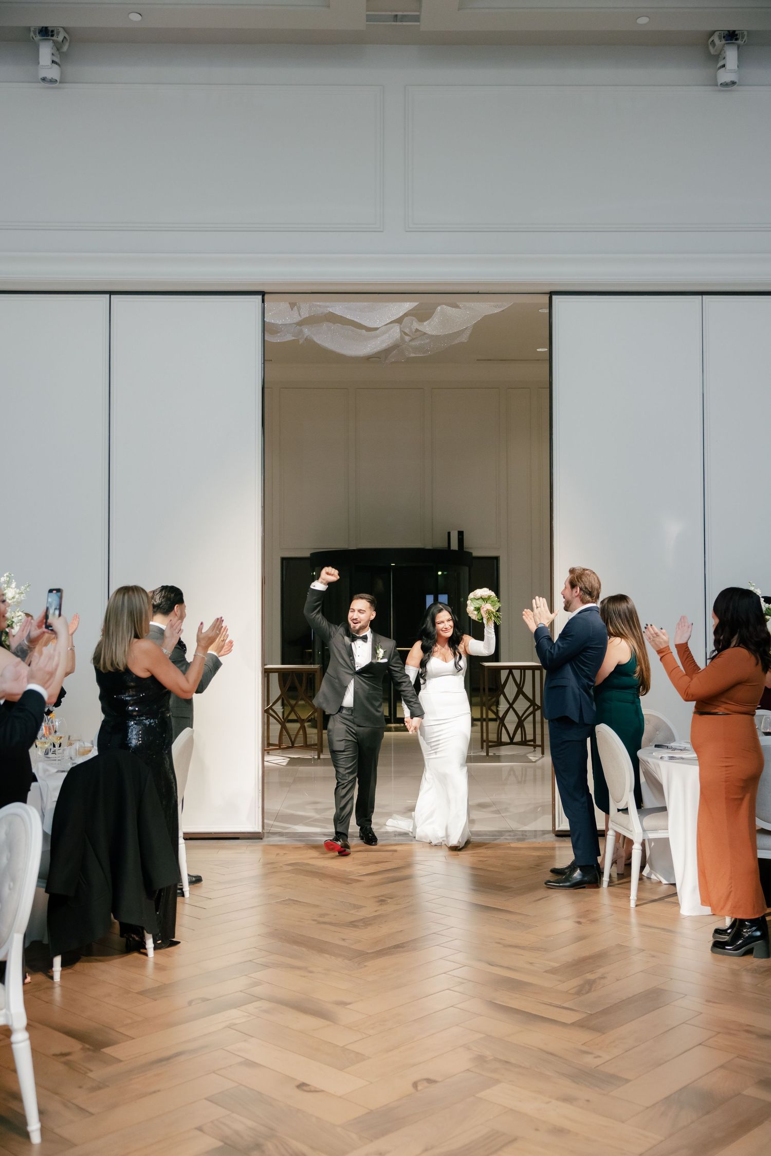 Wedding couple makes grand entrance through white sliding doors as guests applaud.