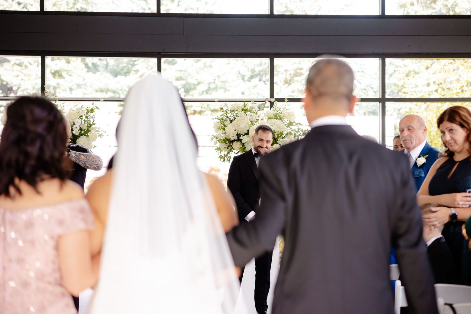 Wedding ceremony in progress inside a modern venue with large windows and natural light.