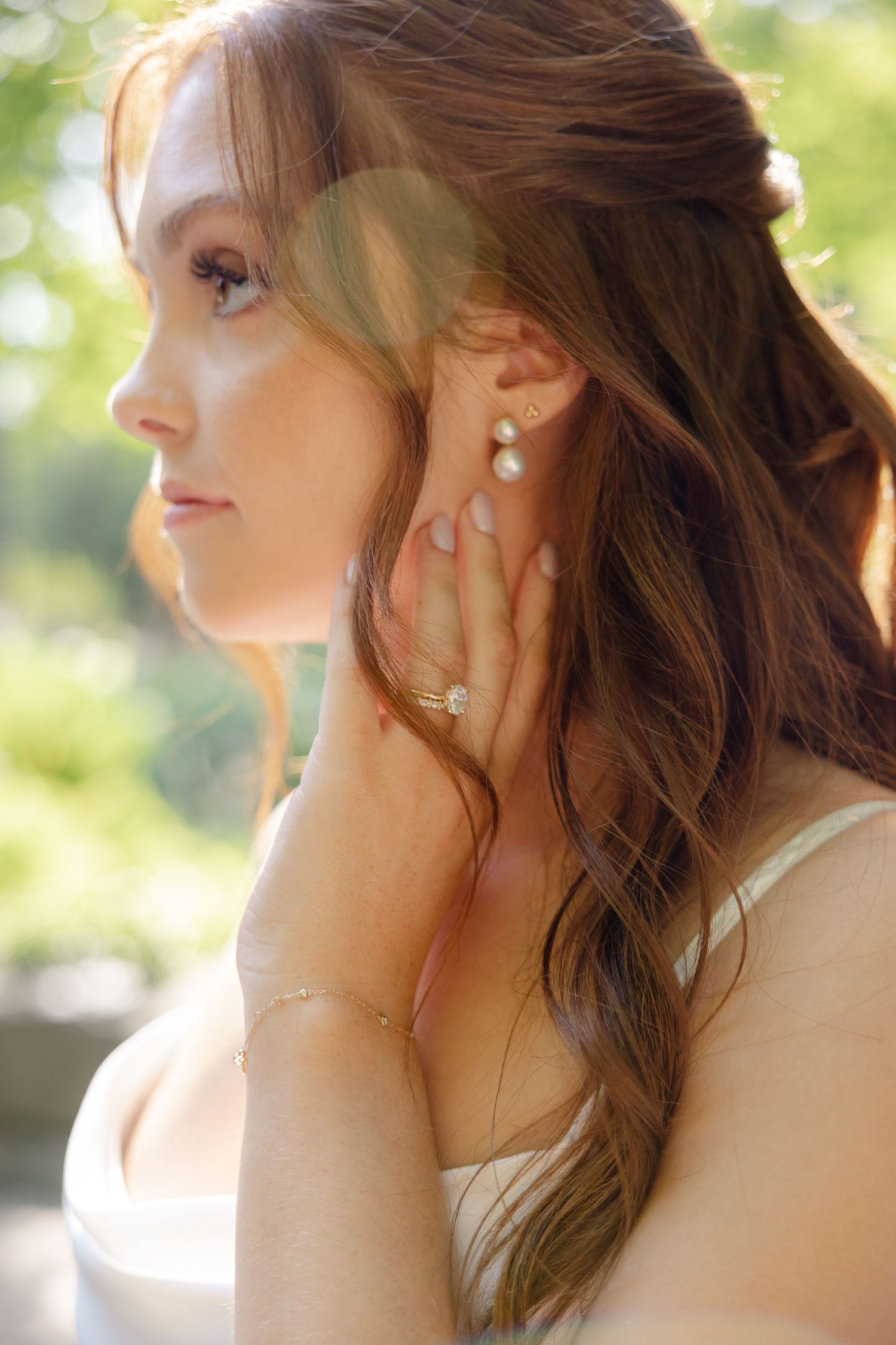 A bride in natural lighting shows delicate pearl earrings and wavy hair styled for her wedding day.
