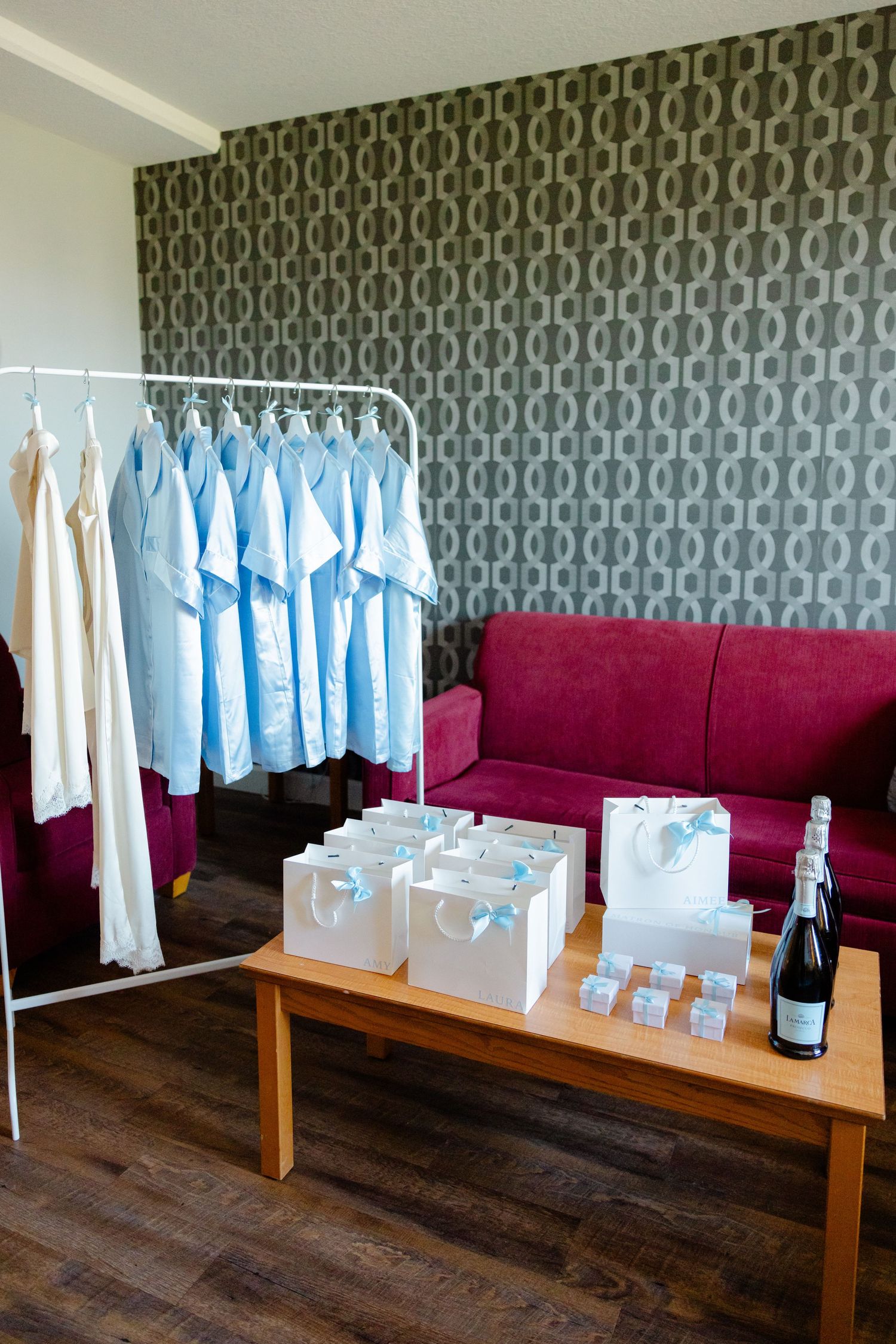 Getting ready room with clothing rack, burgundy couch and wedding favor bags on table.