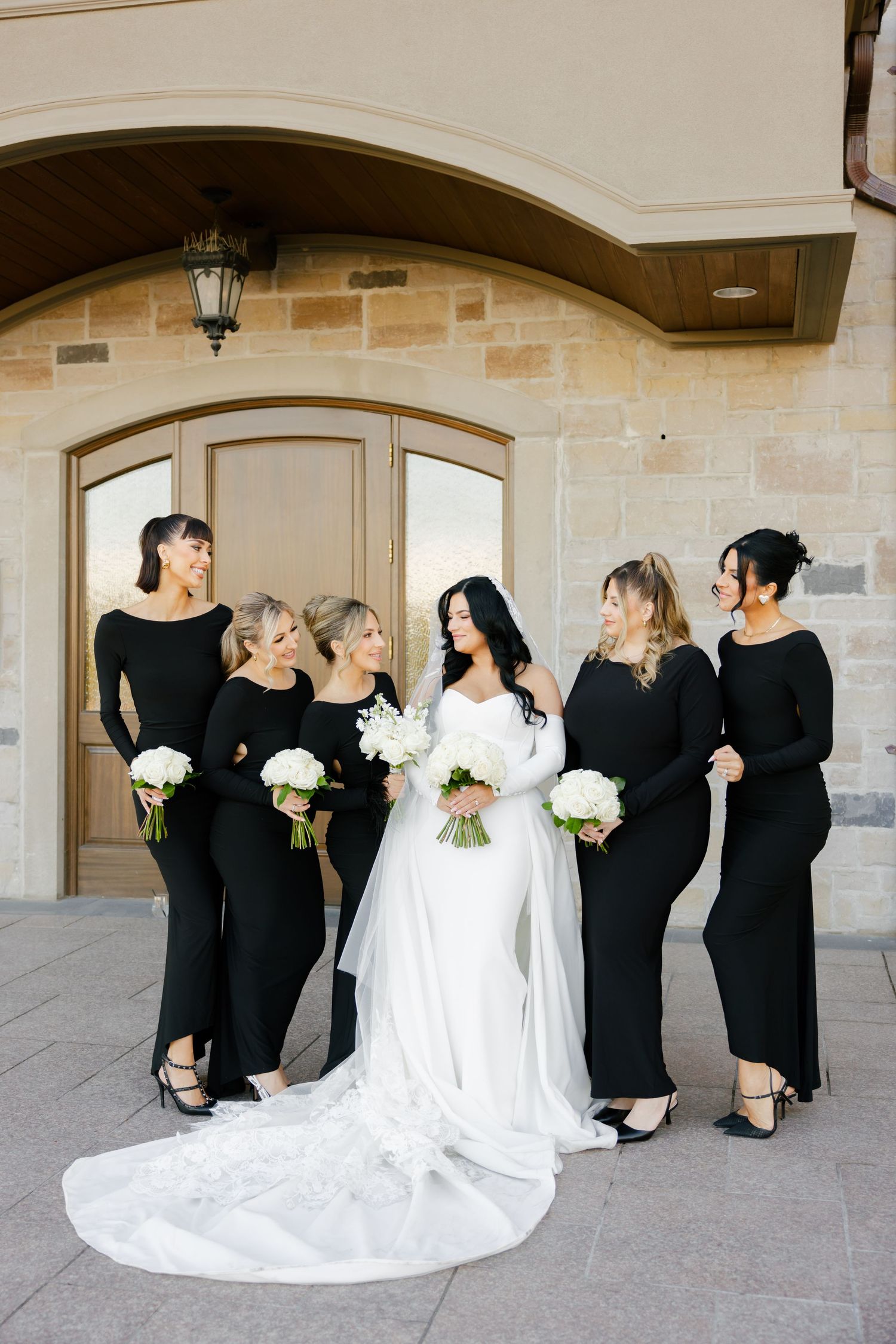 Bridesmaids in matching black dresses share candid moment with bride in white gown.