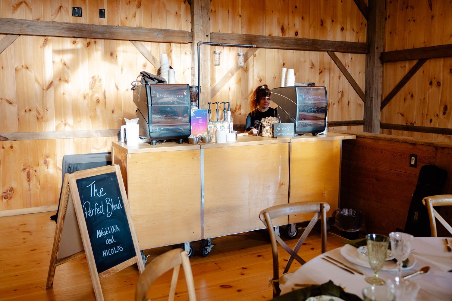 A rustic wooden bar setup with point of sale systems and chalkboard sign in a barn venue.