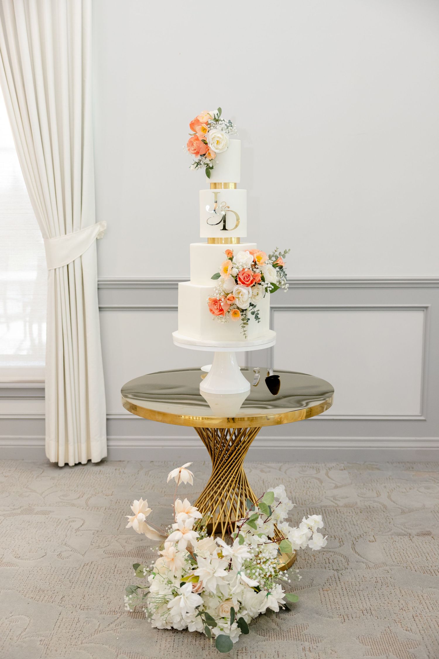 Classic white tiered wedding cake with peach floral accents on gold mirrored cake stand.