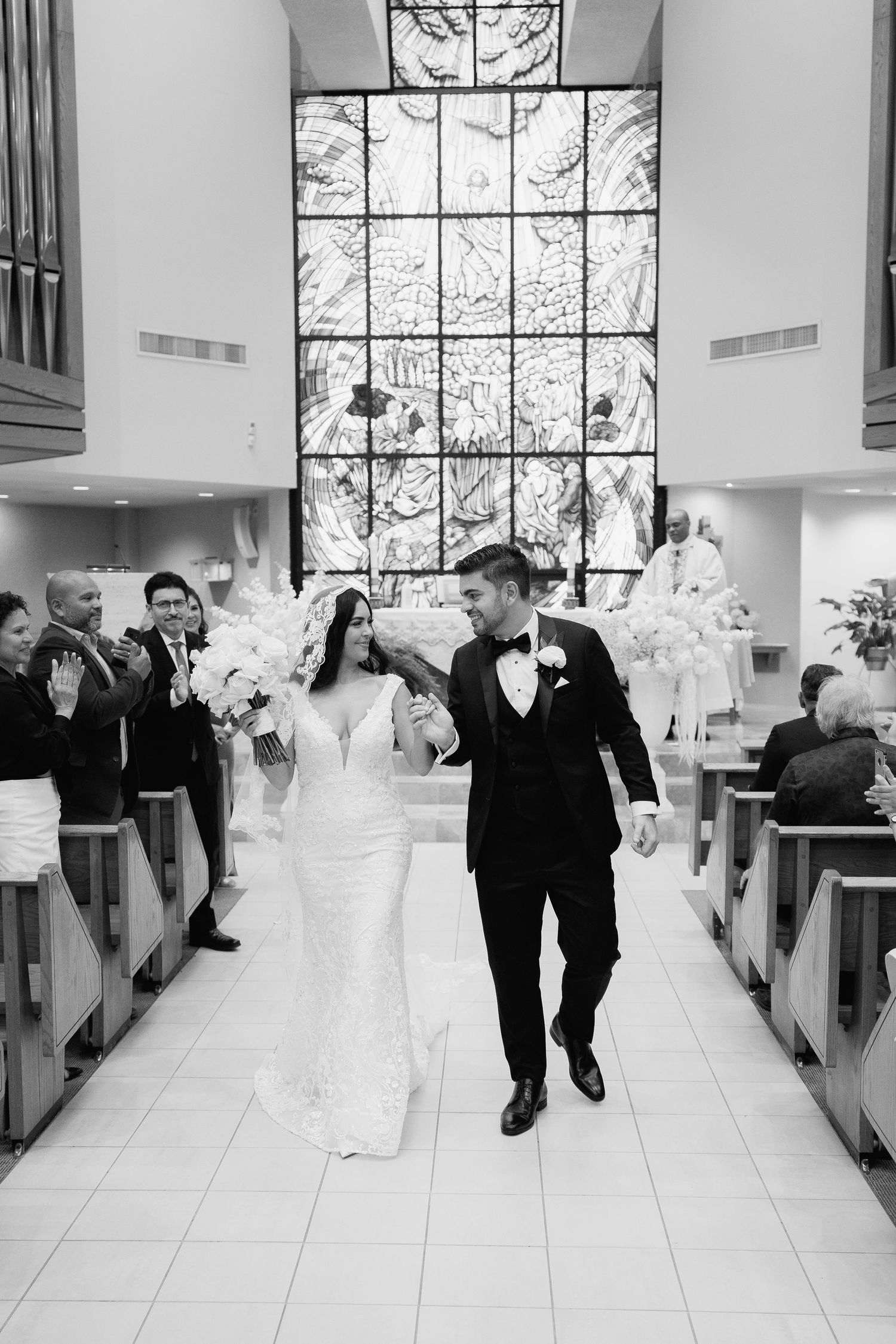 Black and white shot of newlyweds exiting church while guests celebrate.