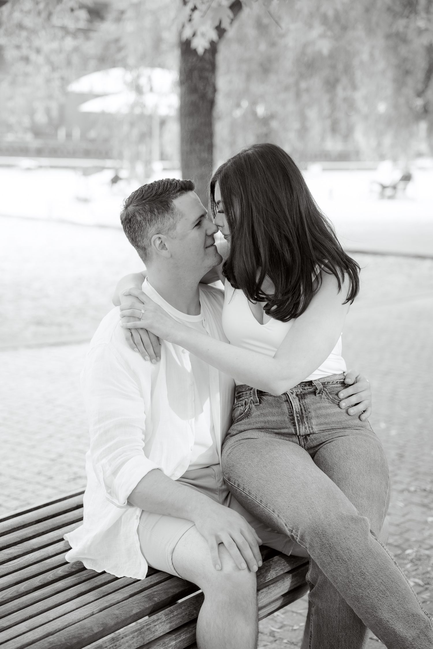 An intimate black and white photo of a couple sharing a close moment on a wooden bench.