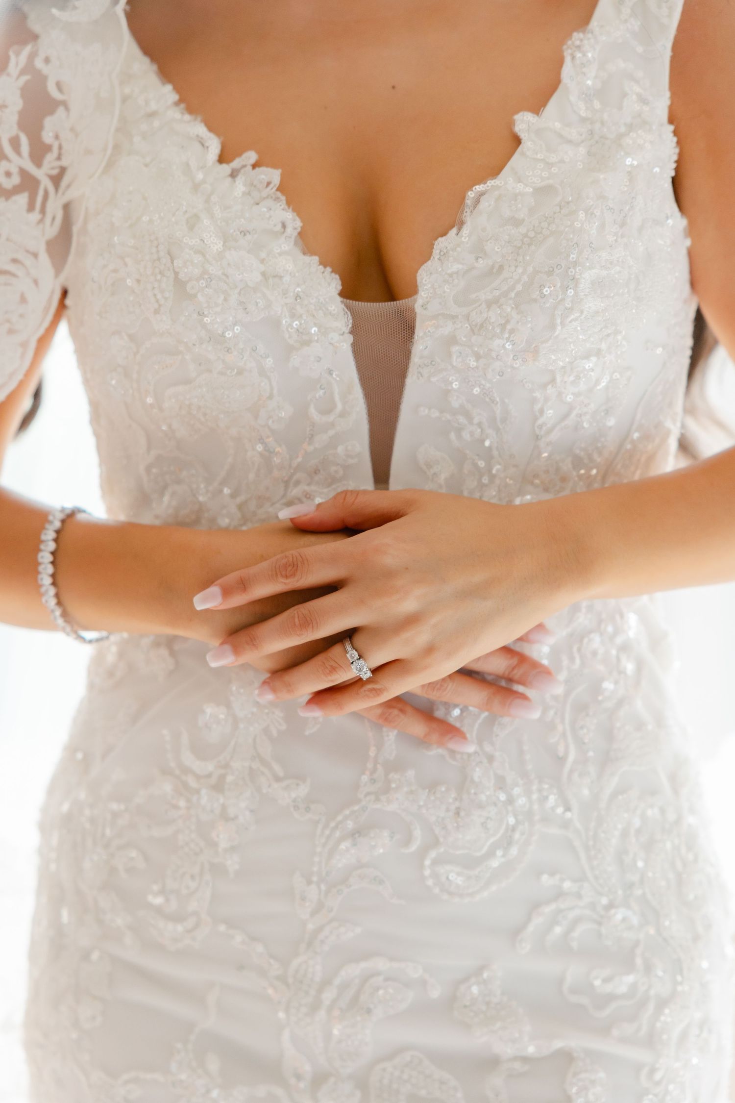 Close up detail of lace wedding dress bodice with deep v-neck and jewelry accents.