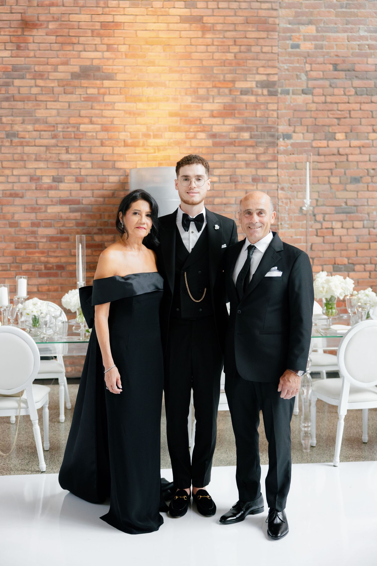Family formal portrait at elegant wedding reception with exposed brick backdrop.