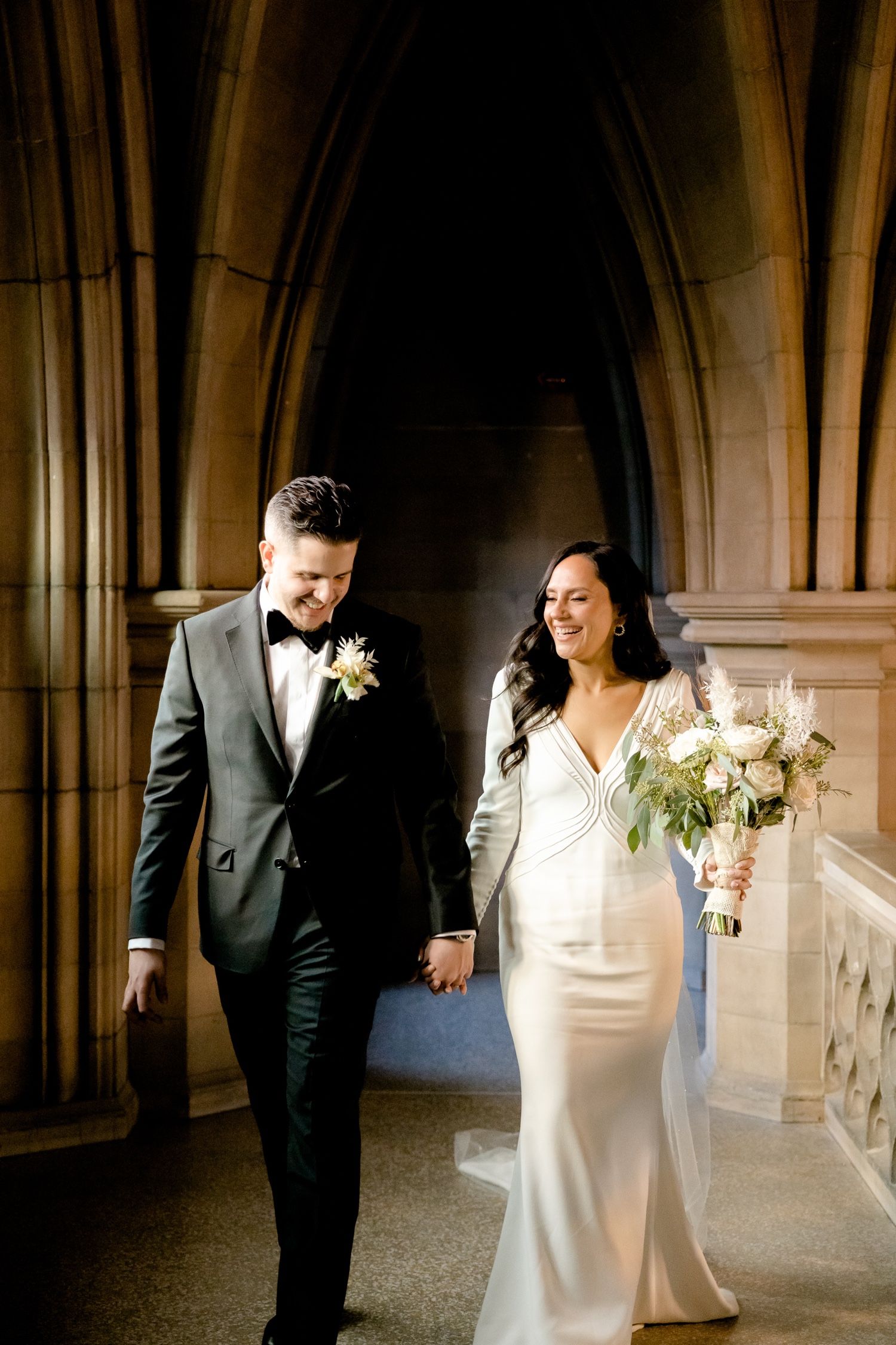 Newlyweds share a joyful moment in a cathedral corridor with stunning architectural details.