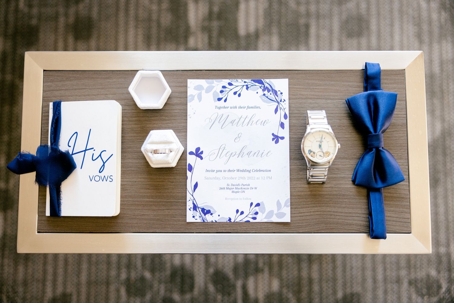 Wedding details flat lay with blue bow tie, invitation, and white hexagonal decorative elements.