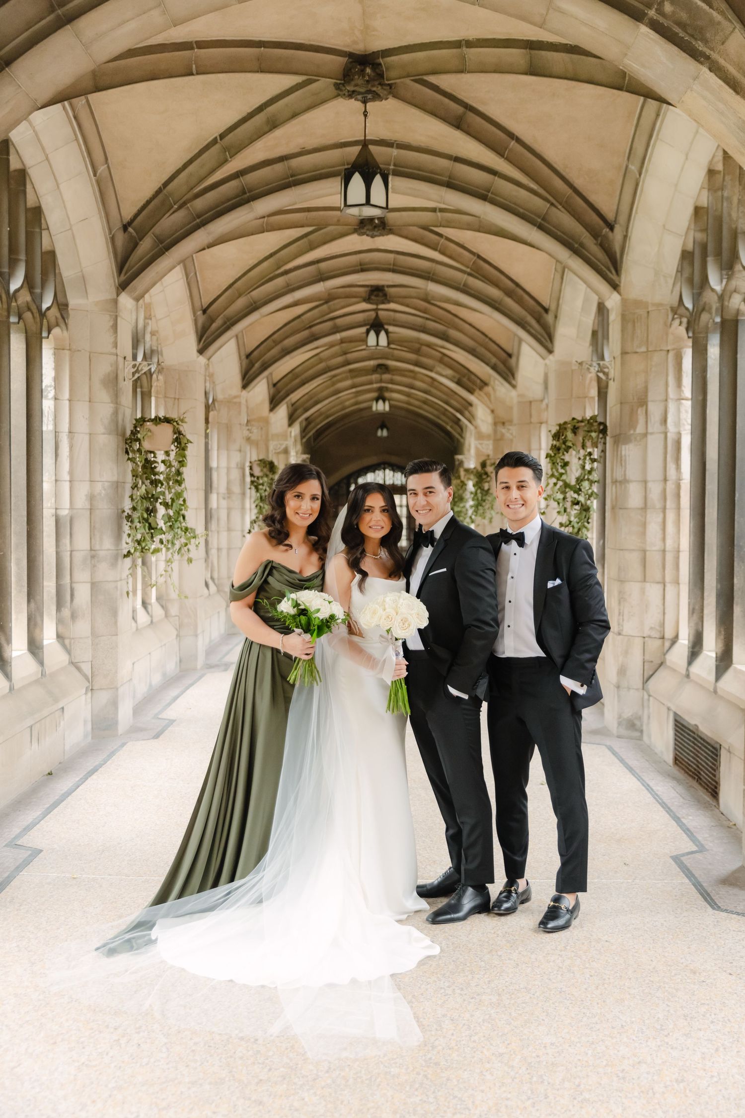 Wedding party of four poses in formal attire under ornate Gothic architecture.