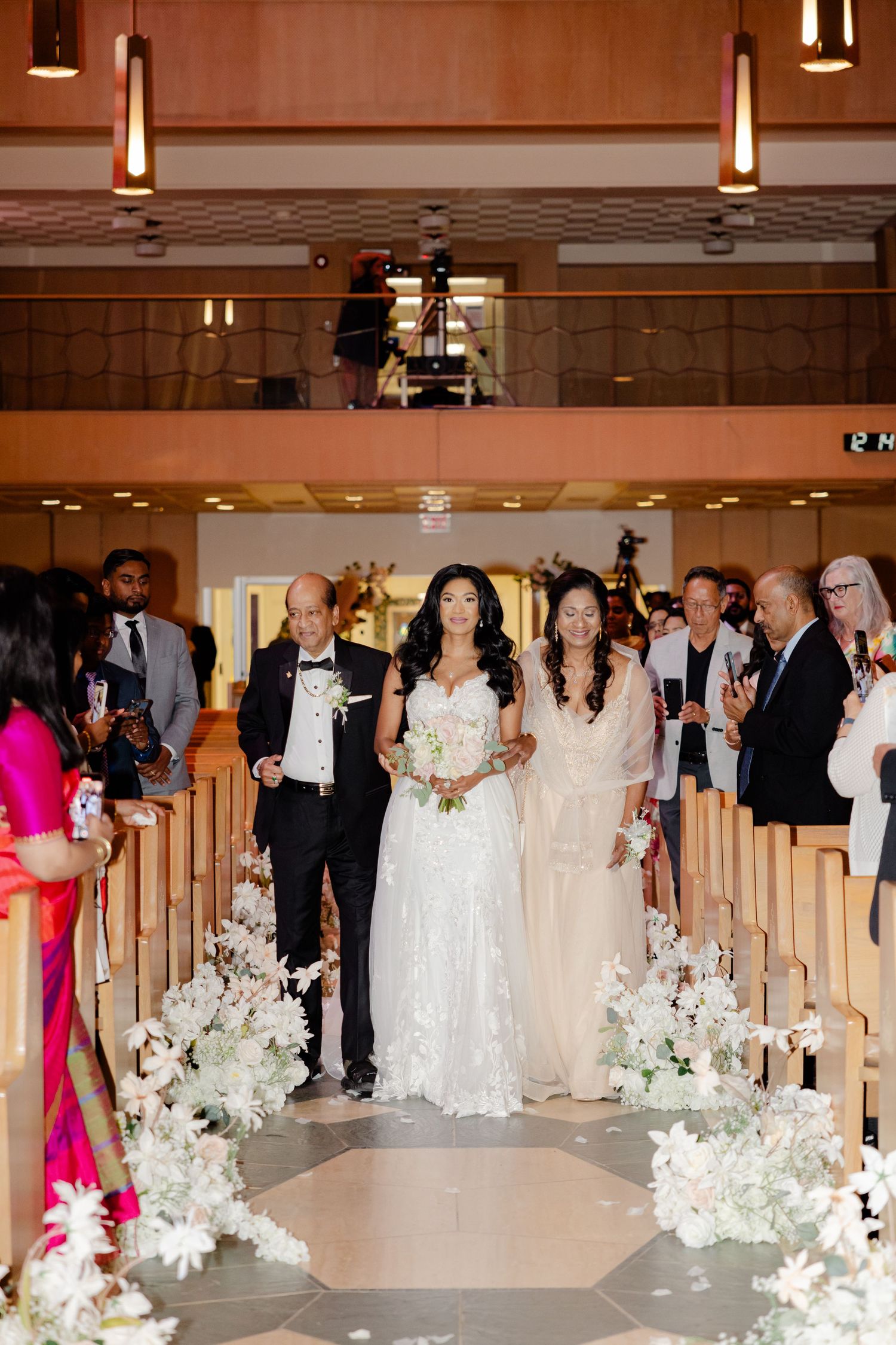 Wedding processional in a church sanctuary with beautiful white floral decorations lining the aisle.