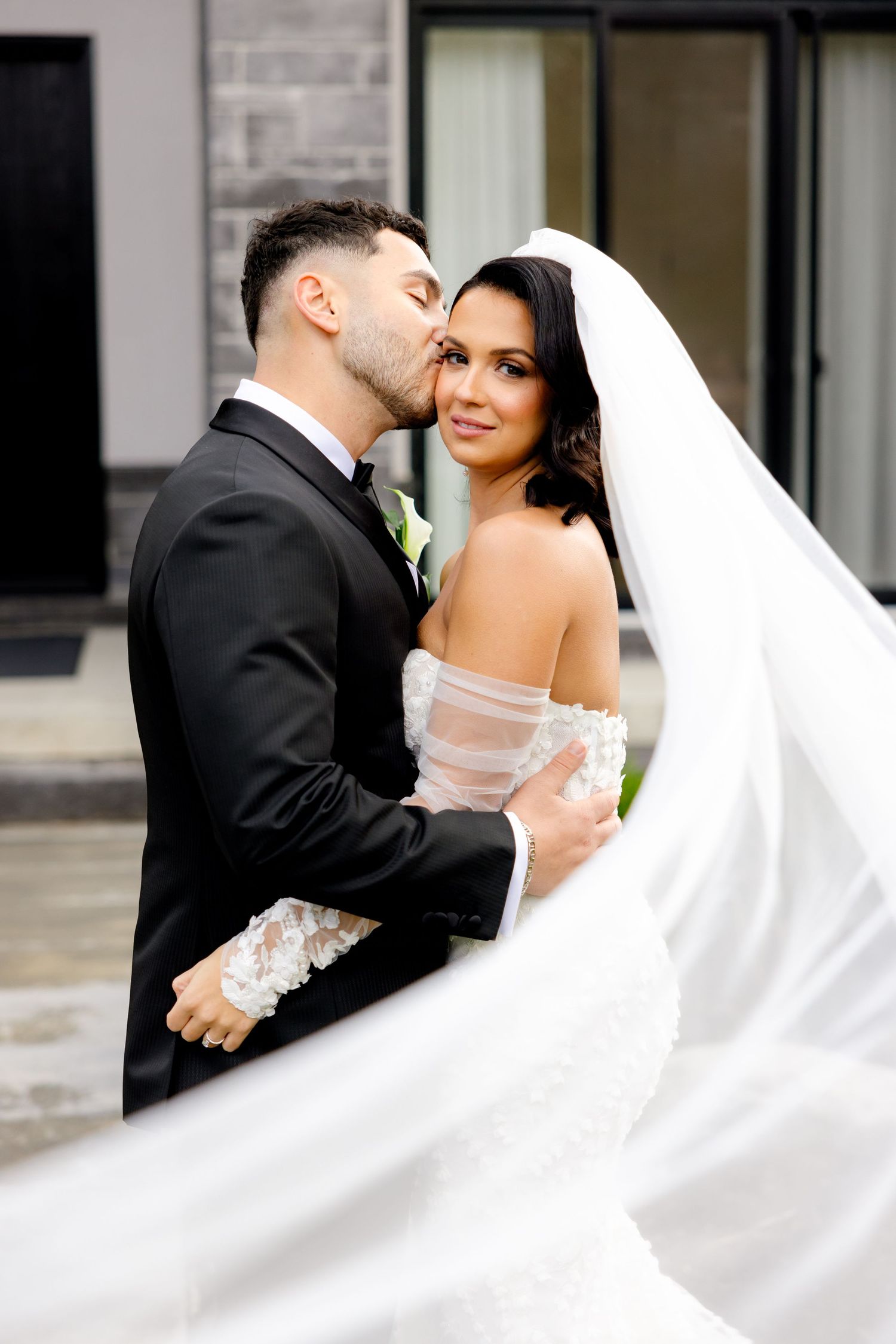 Romantic wedding portrait with flowing white veil and modern architecture backdrop.