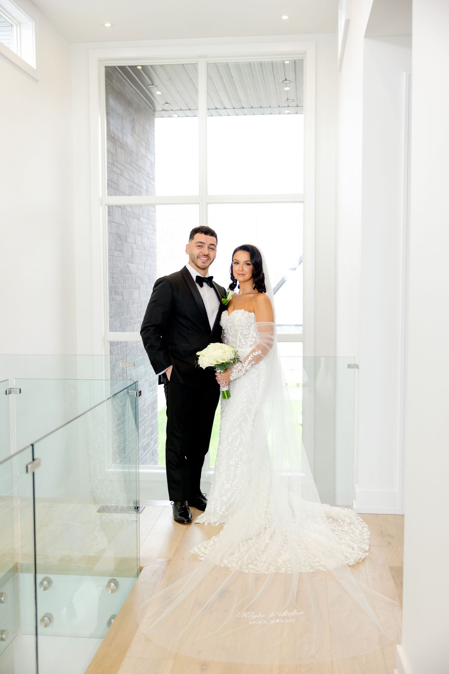 Wedding couple standing in modern white hallway with glass railing and natural light.