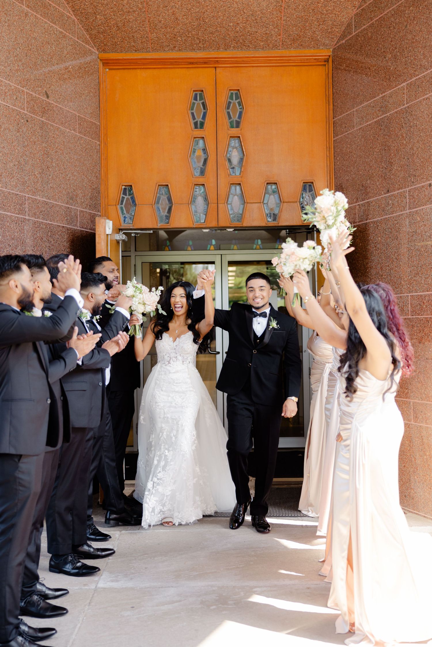 Wedding party lines up for celebratory exit photos at church entrance with decorative wall fixtures.