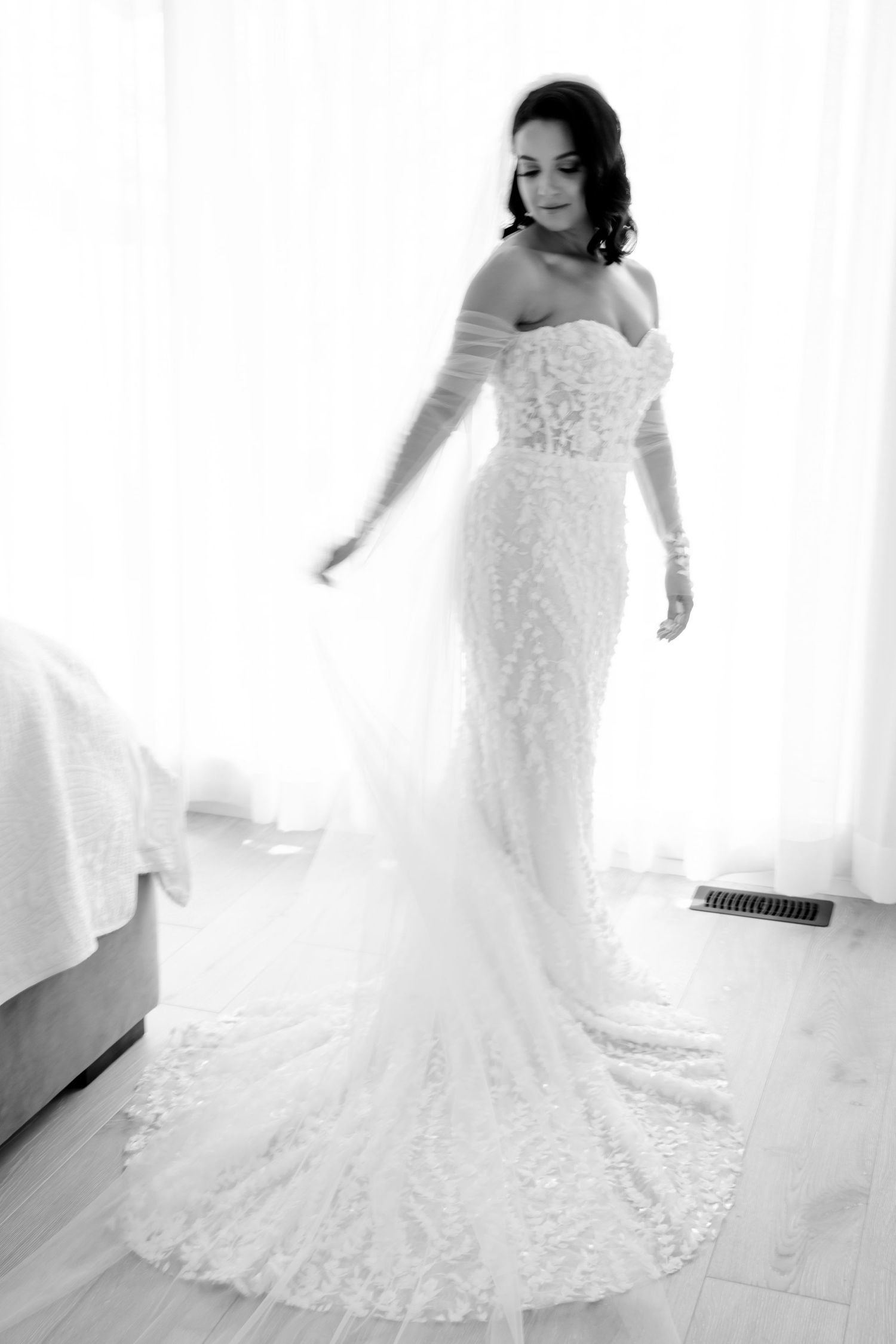 A stunning off-shoulder lace wedding gown with a fitted silhouette and dramatic train in black and white photography.