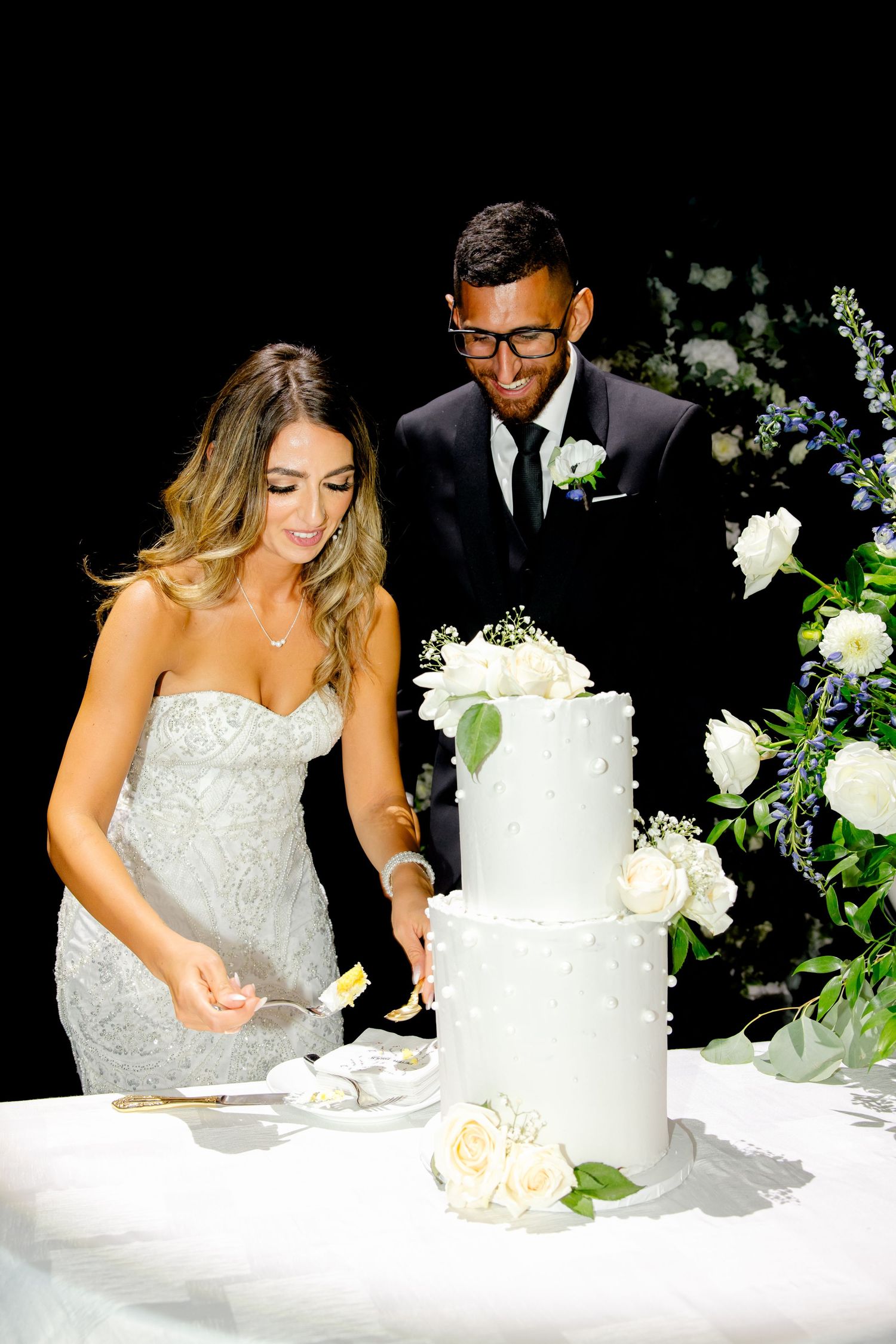 Couple sharing a moment while cutting their elegant white tiered wedding cake.