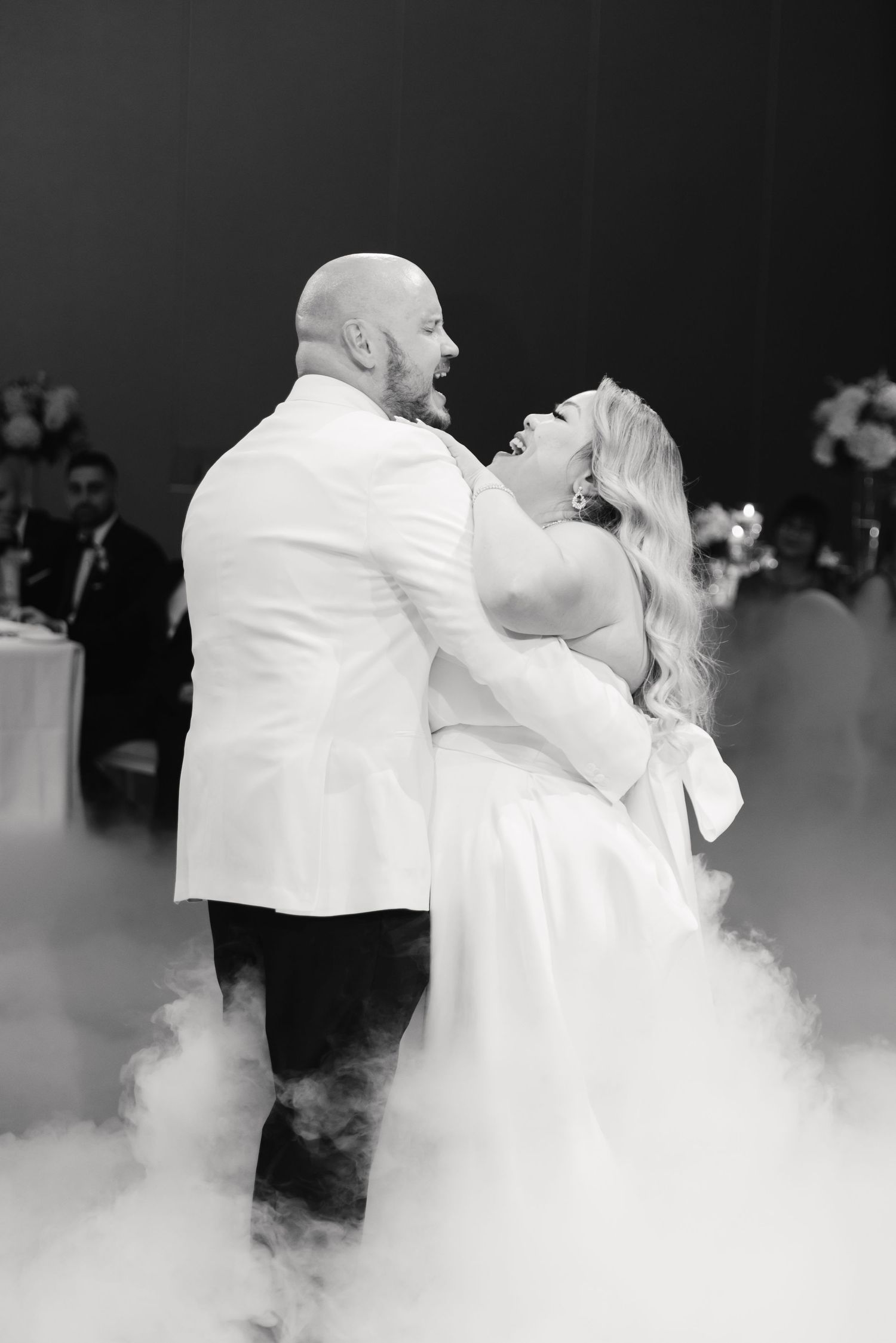 Newlyweds share their first dance on a fog-covered dance floor during their wedding reception.