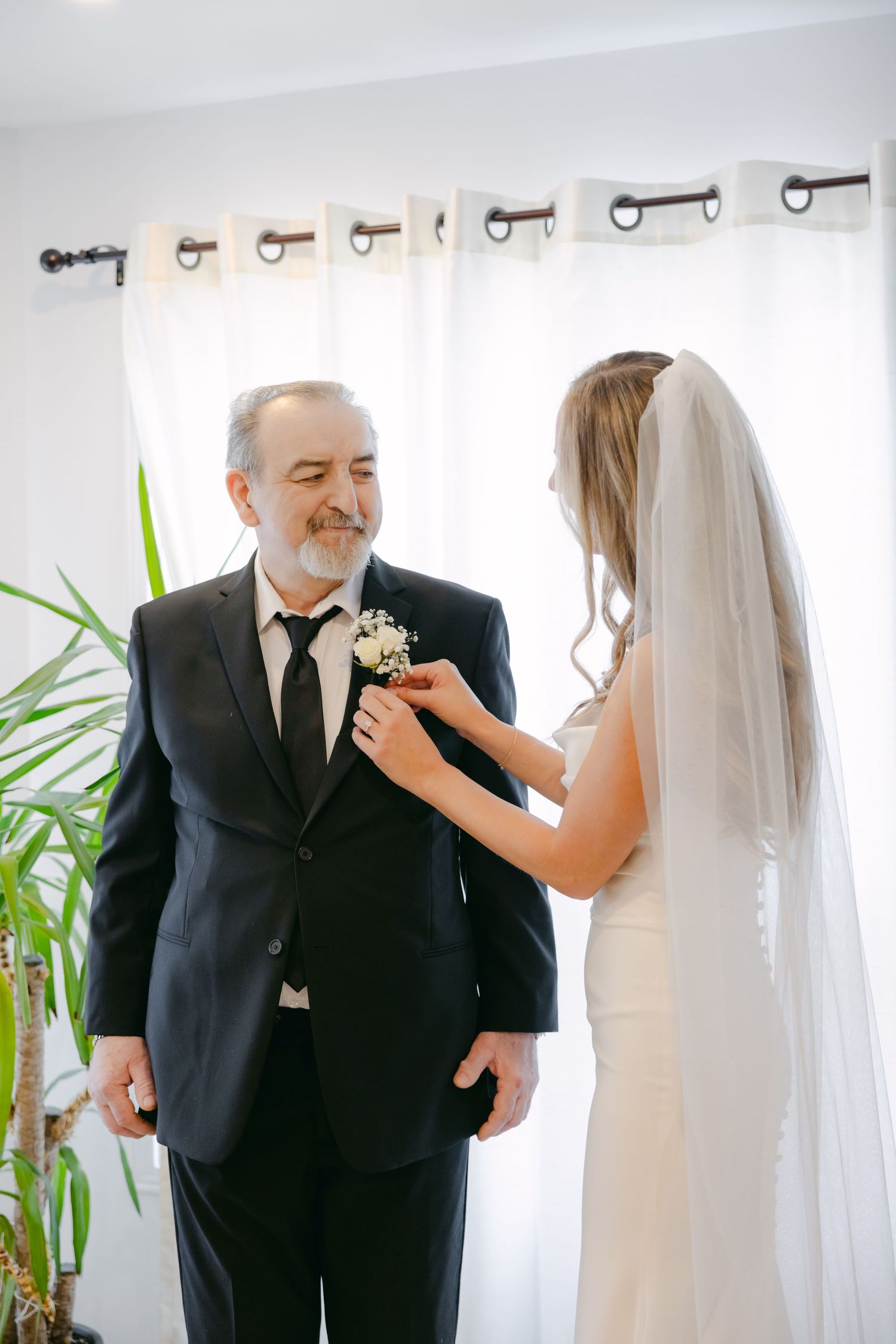 A touching pre-wedding moment unfolds by a bright window with white curtains.