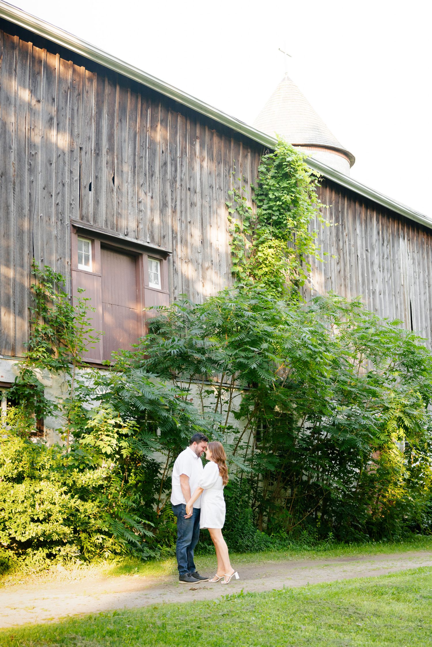 A romantic moment captured between a couple by an old wooden barn with climbing vines.