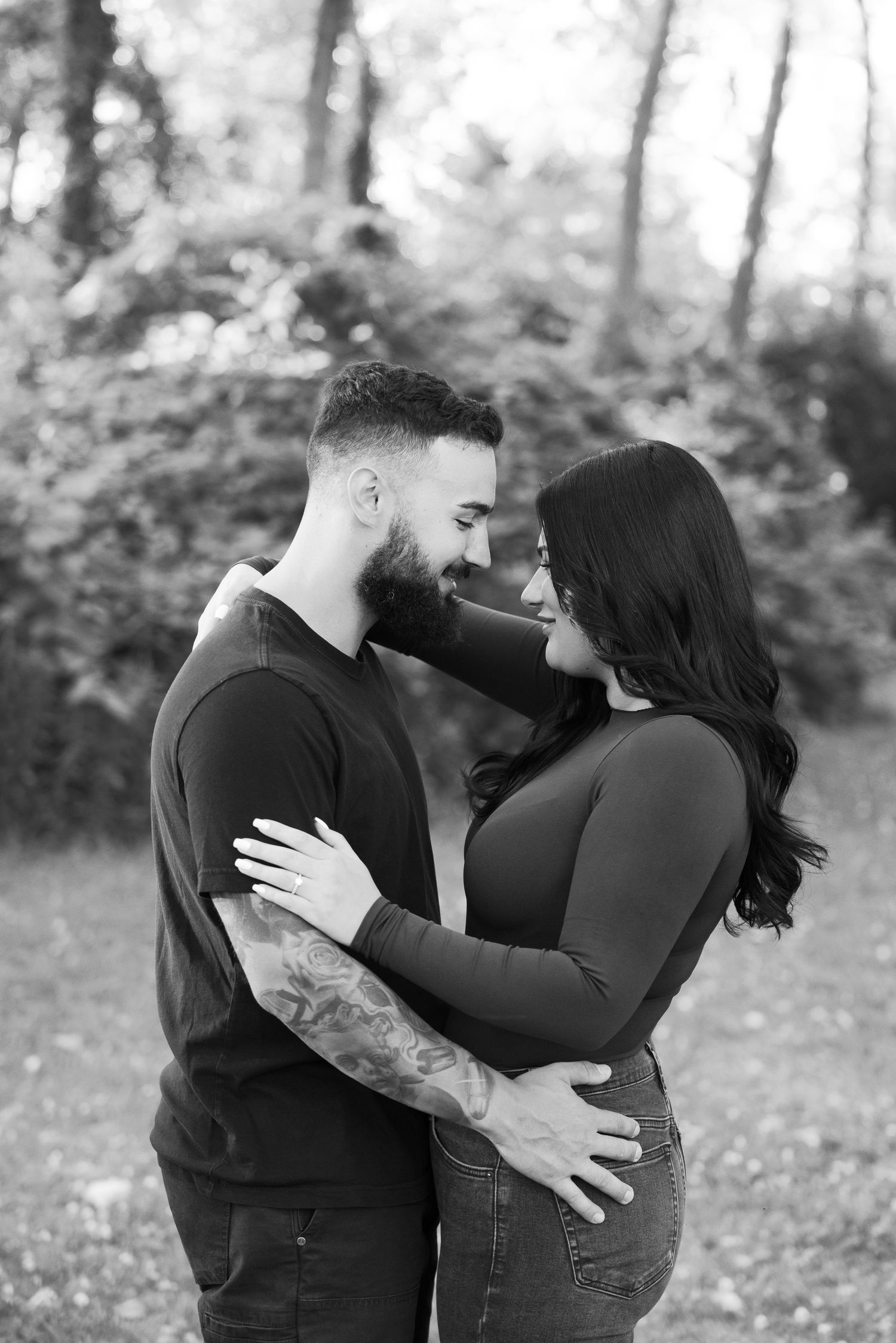 Black and white portrait of a couple in a tender embrace against a forest backdrop.
