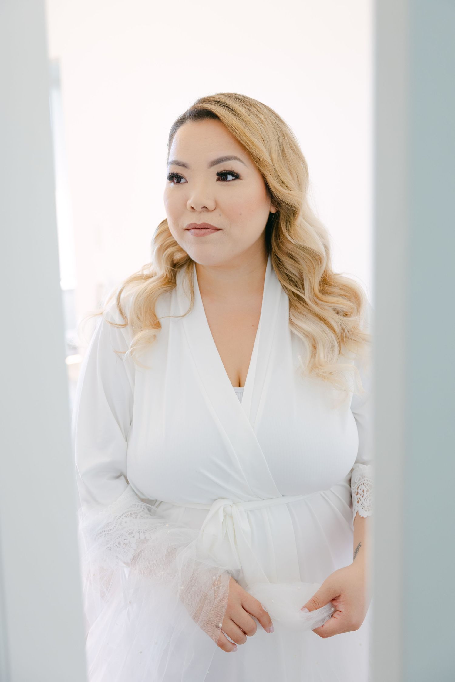 Bride wearing white robe with blonde wavy hair during wedding day preparations.