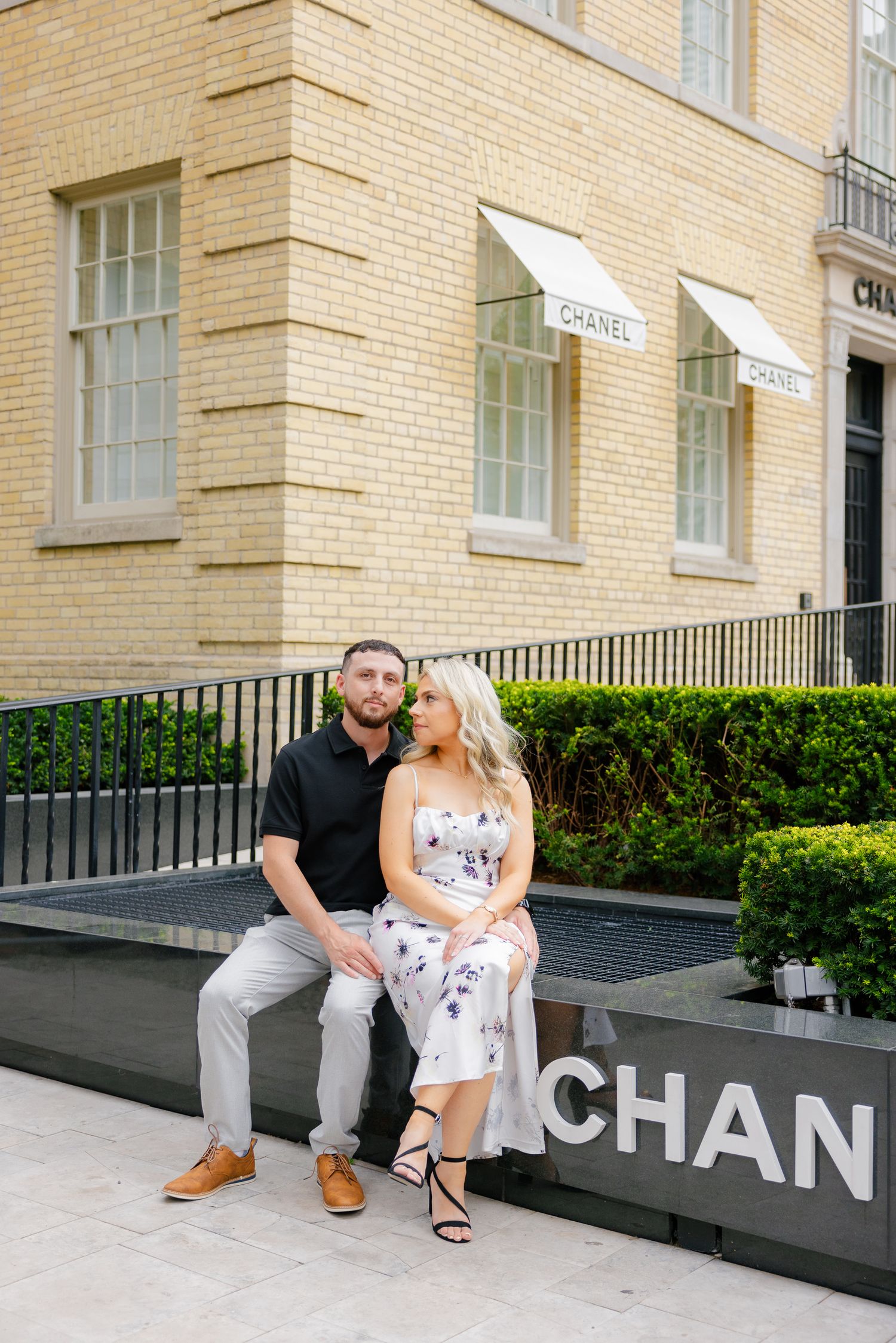 Couple sitting together on ledge outside Chanel boutique in coordinated outfits.