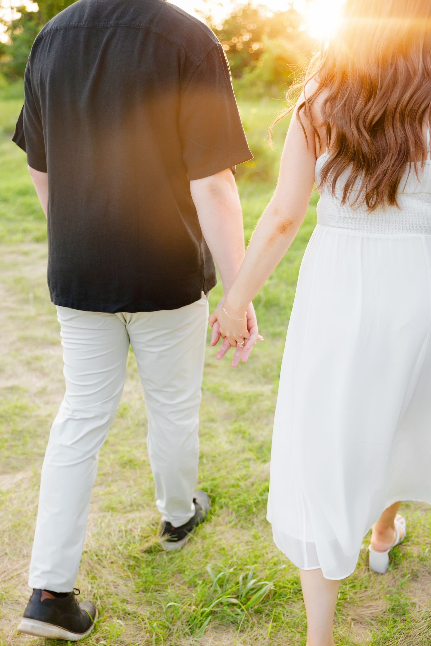 Close-up of couple holding hands while walking in sunlit park setting.