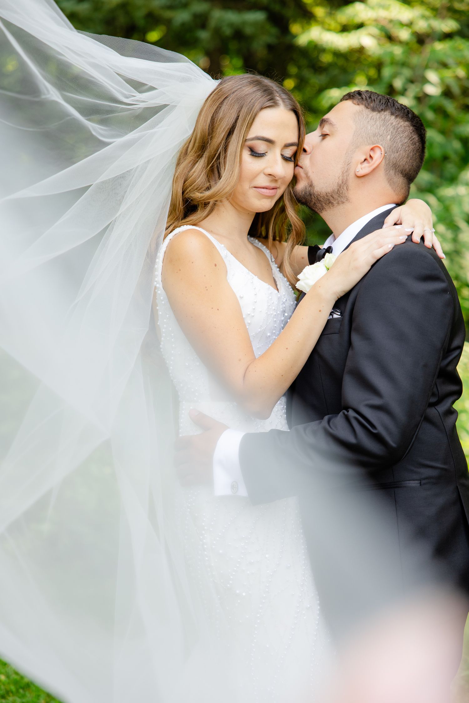 A romantic wedding portrait featuring a flowing veil and intimate embrace in a garden setting.