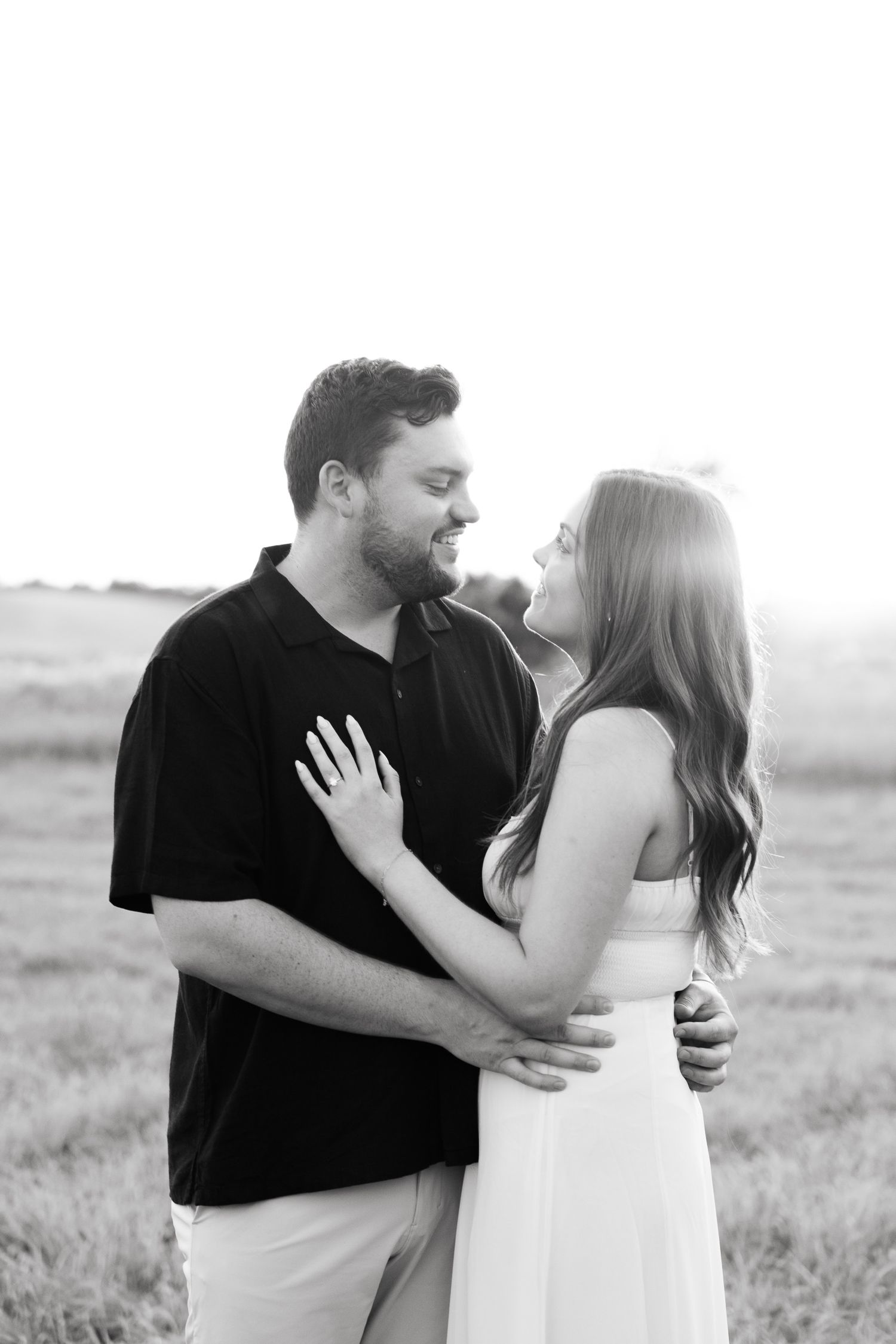 Black and white portrait of couple sharing intimate moment in open field.