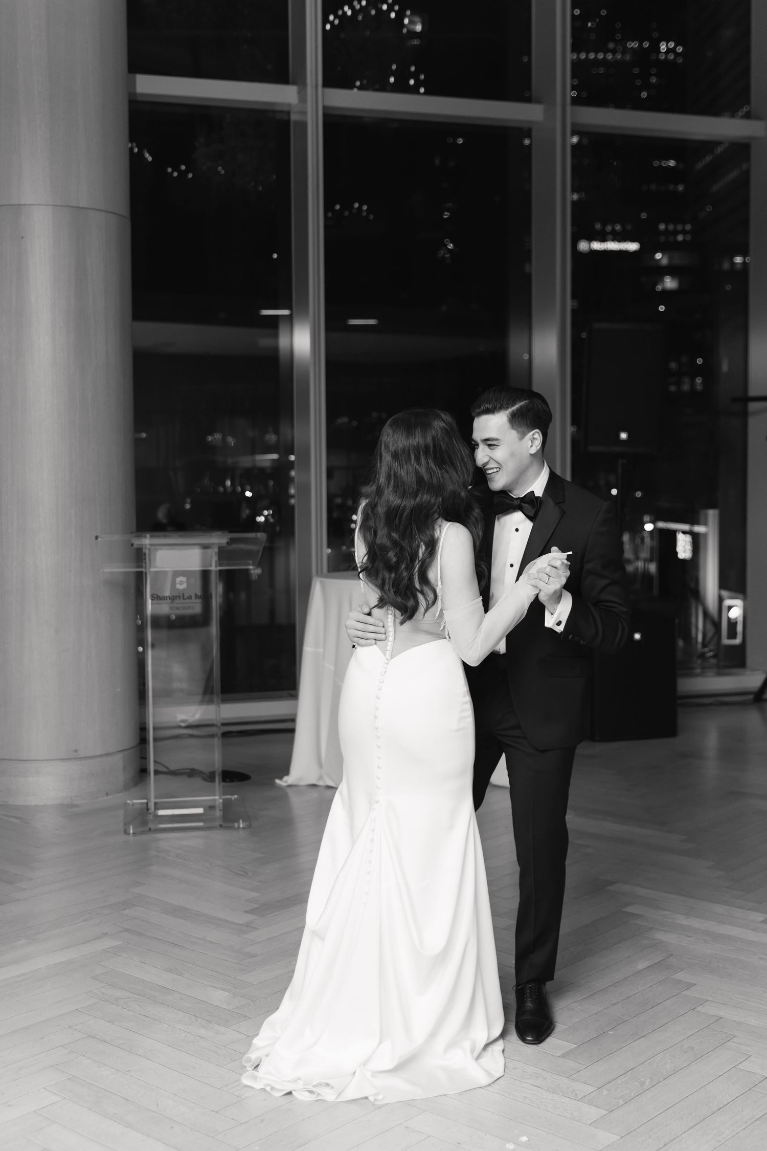 Black and white photo captures intimate first dance moment in modern venue with city lights.