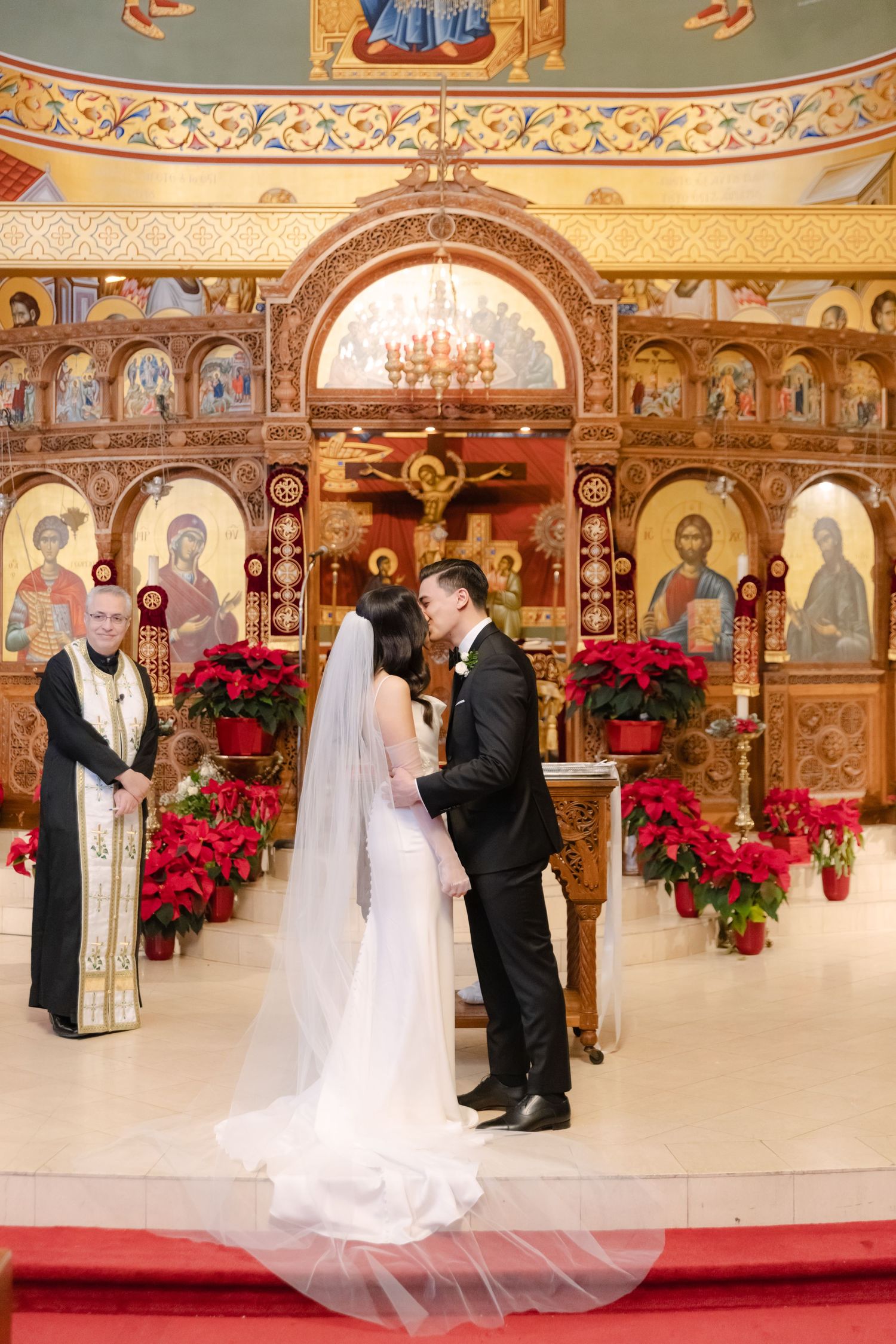 Orthodox wedding ceremony in front of an elaborate iconostasis decorated with red poinsettias.