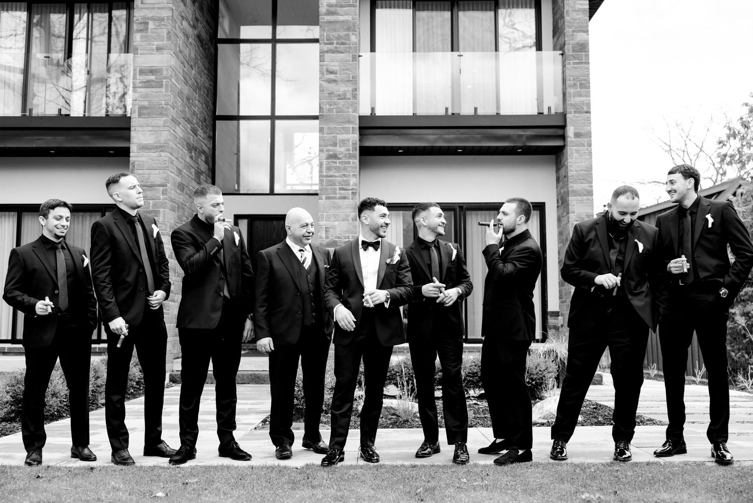 Black and white photo of groomsmen standing in a line outside a modern building.