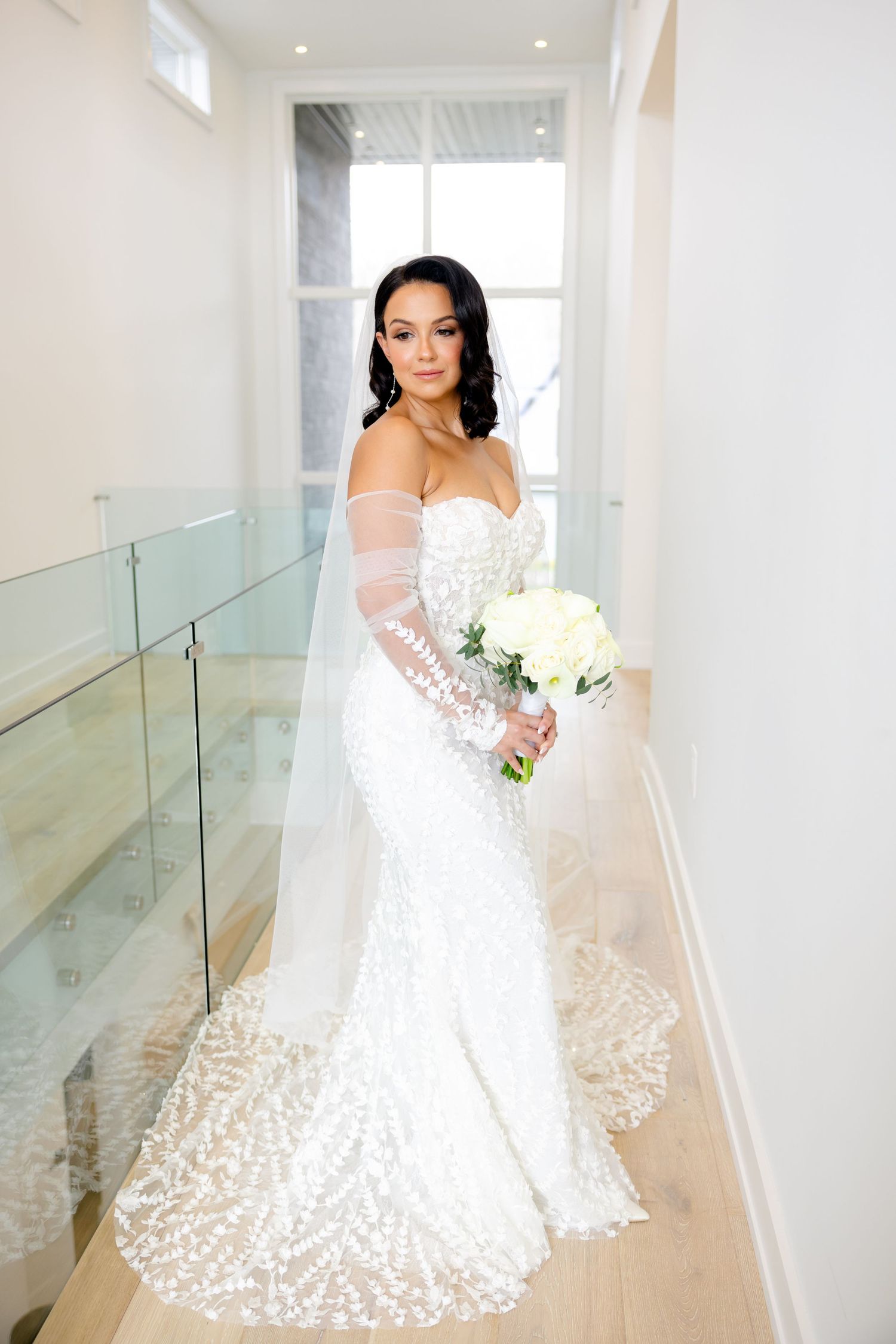 Side view of bride in sweetheart neckline wedding dress holding white bouquet in bright hallway.
