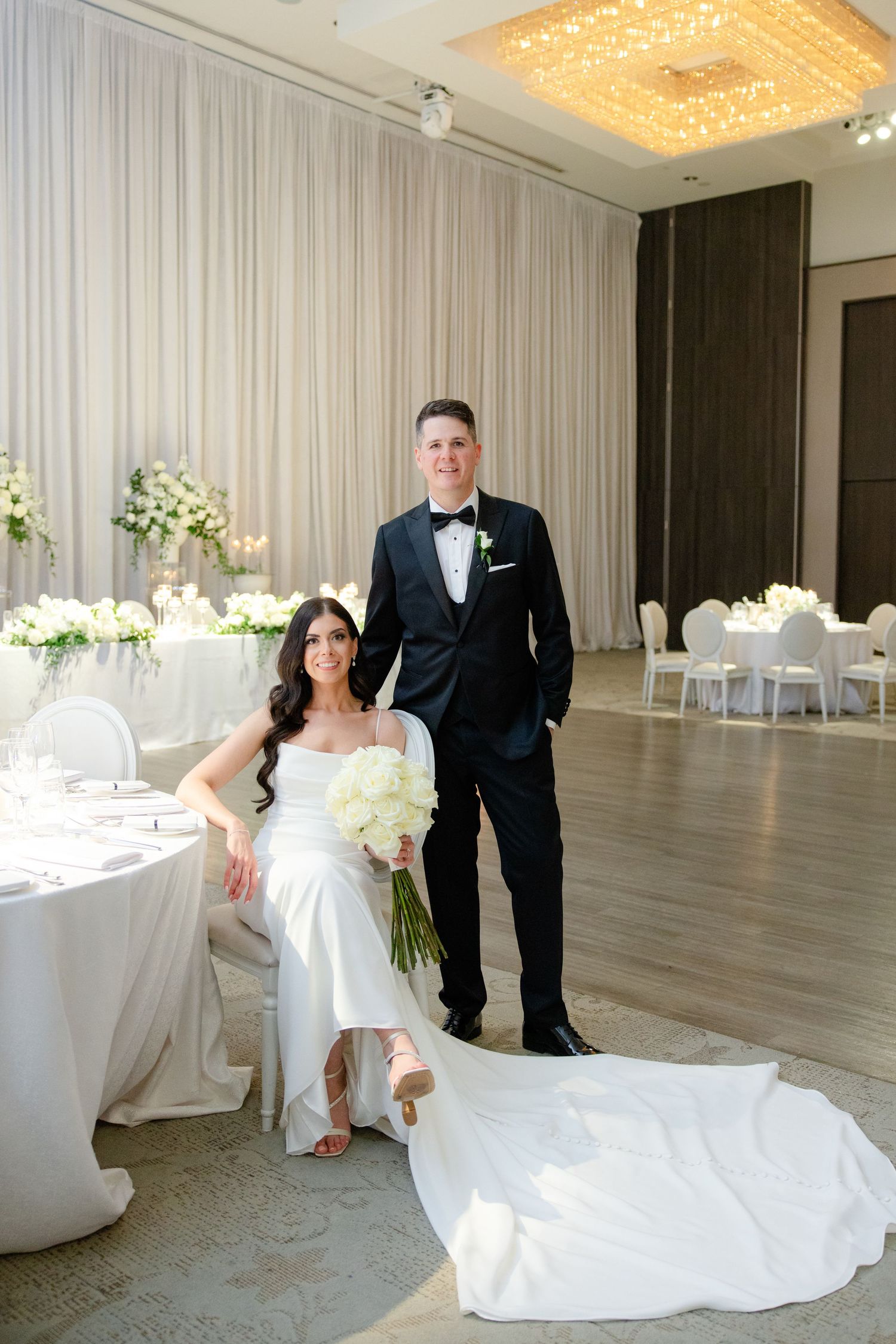 Stylish wedding portrait in modern reception space with crystal chandeliers and white decor.