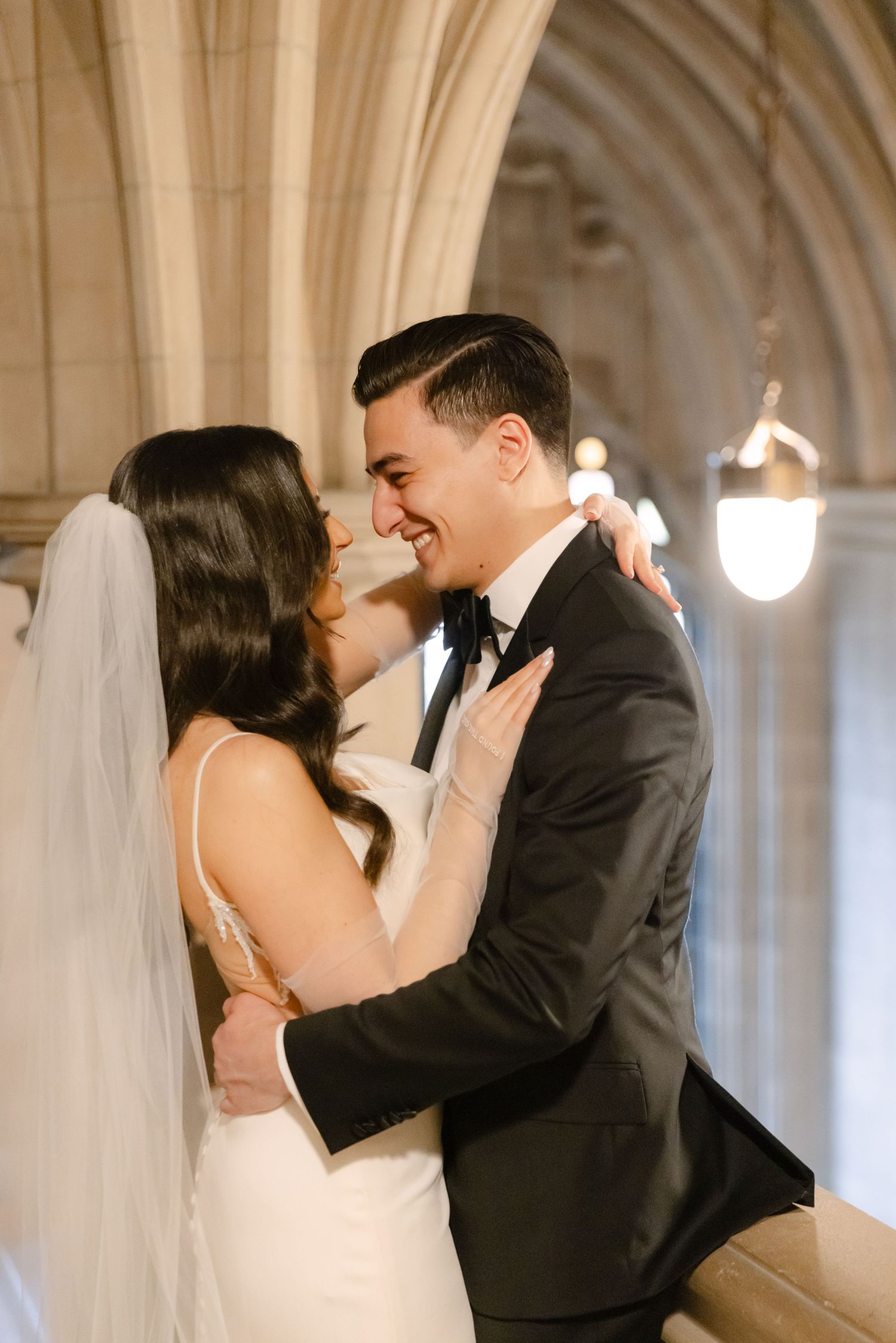 Happy wedding couple shares loving embrace under Gothic stone arches.