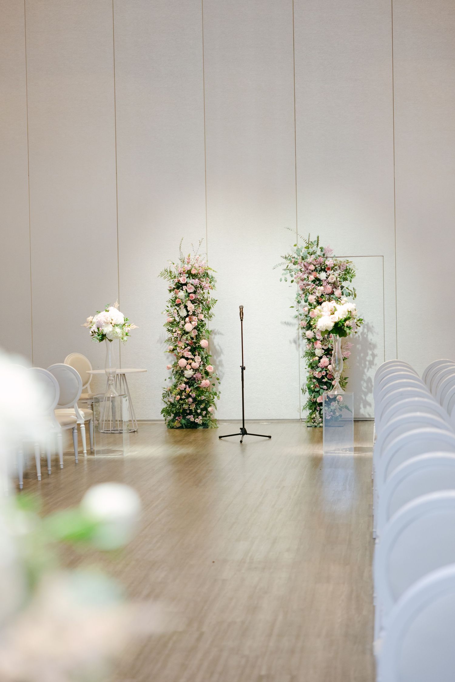 Wedding ceremony setup with white chairs and floral arch arrangements in an elegant indoor space.