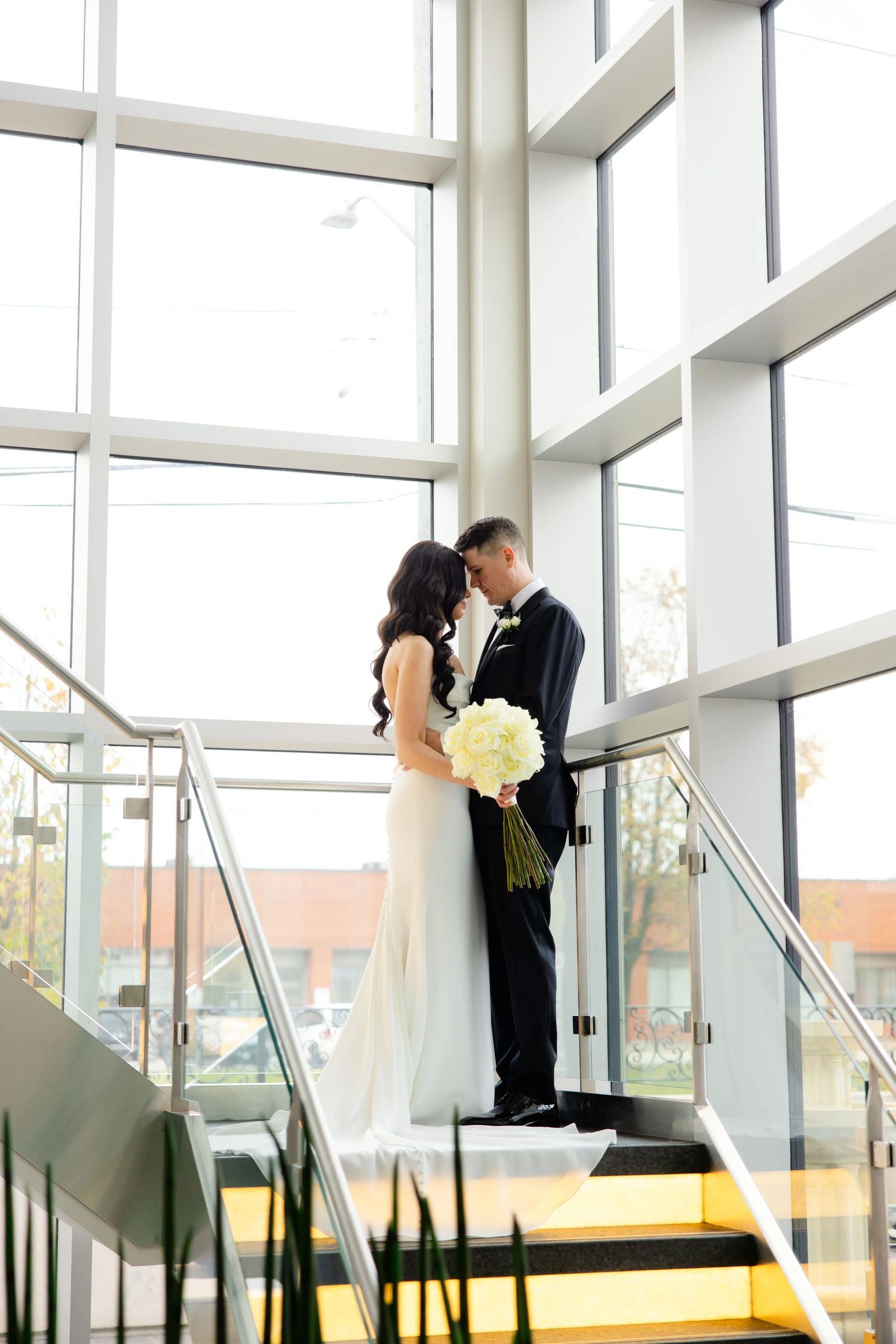 A romantic moment captured on yellow stairs with white bouquet against bright modern windows.