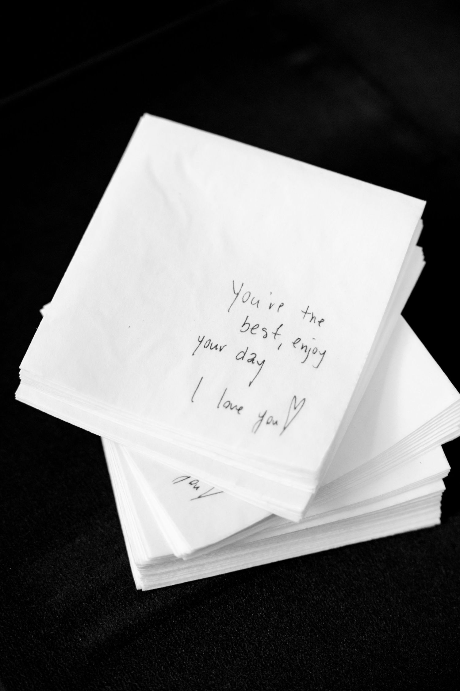 Handwritten love note on white napkins with heartfelt message against dark background.