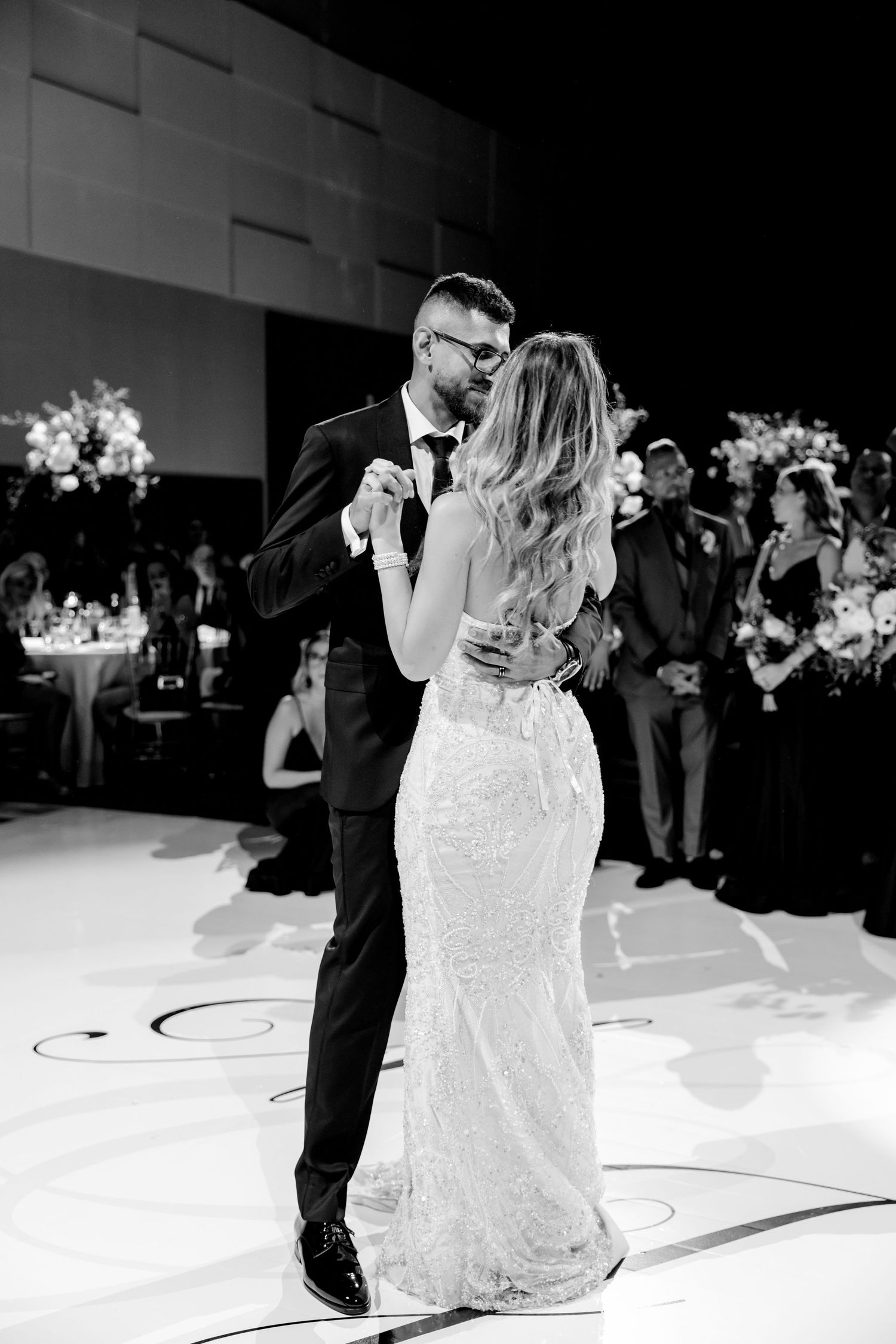 Intimate black and white photo of couple's first dance in fitted wedding attire.