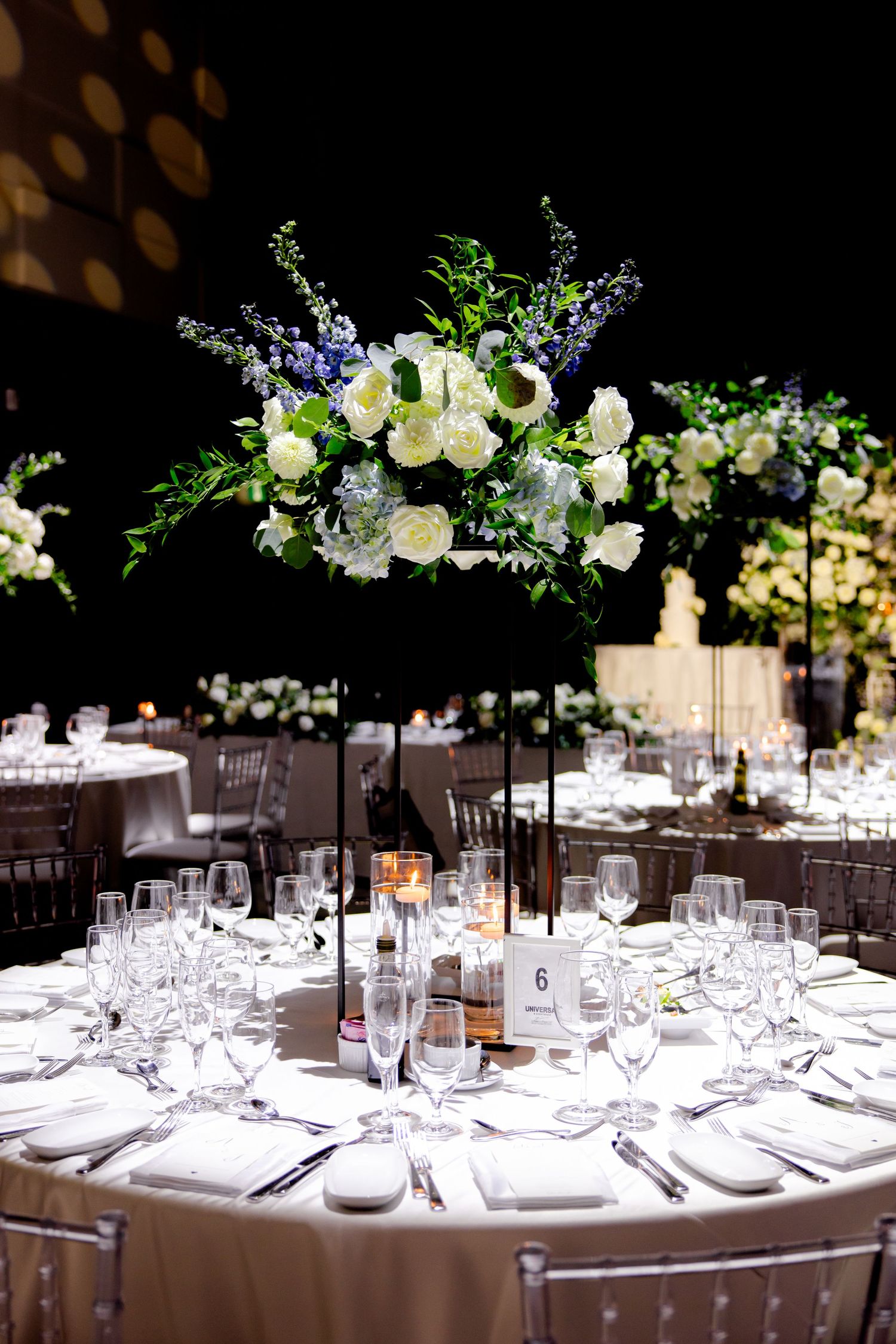 Round wedding reception table with tall white and purple floral centerpiece and elegant place settings.