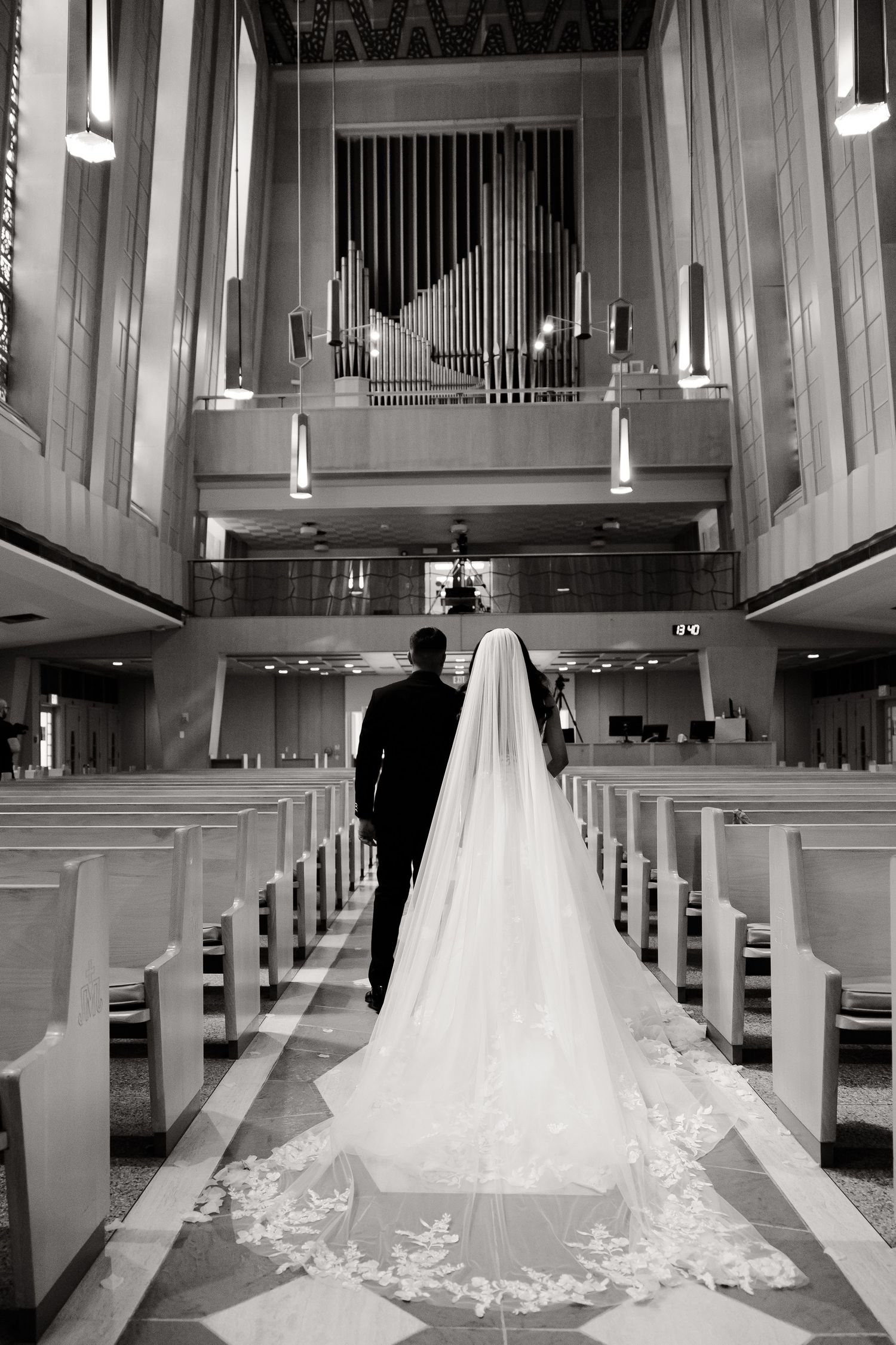 Long cathedral aisle with pipe organ and wooden pews in black and white.