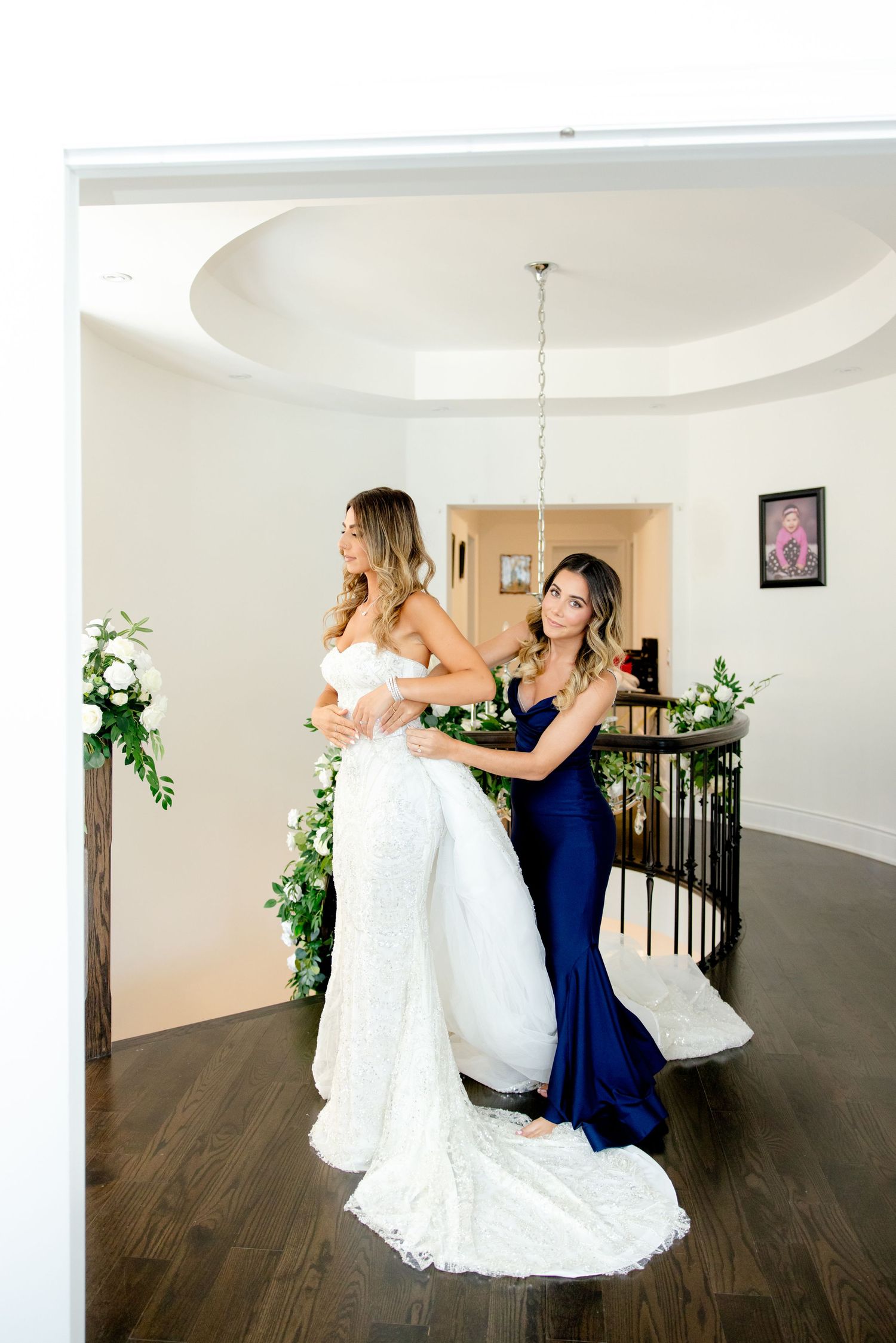 Candid behind-the-scenes moment of dress adjustments with bride in white gown.
